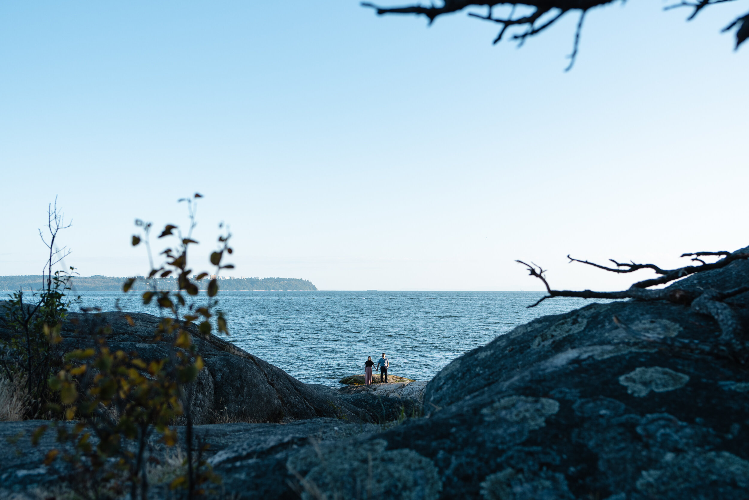 Couple stands on rock next to ocean in distance