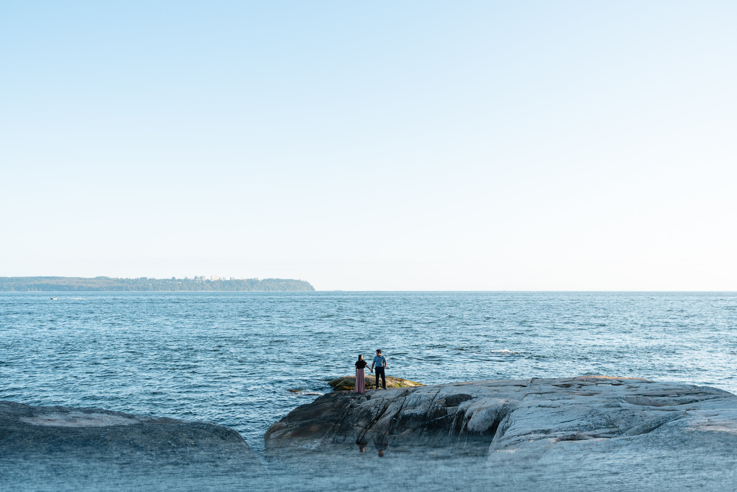 Couple stands on rock next to ocean in distance