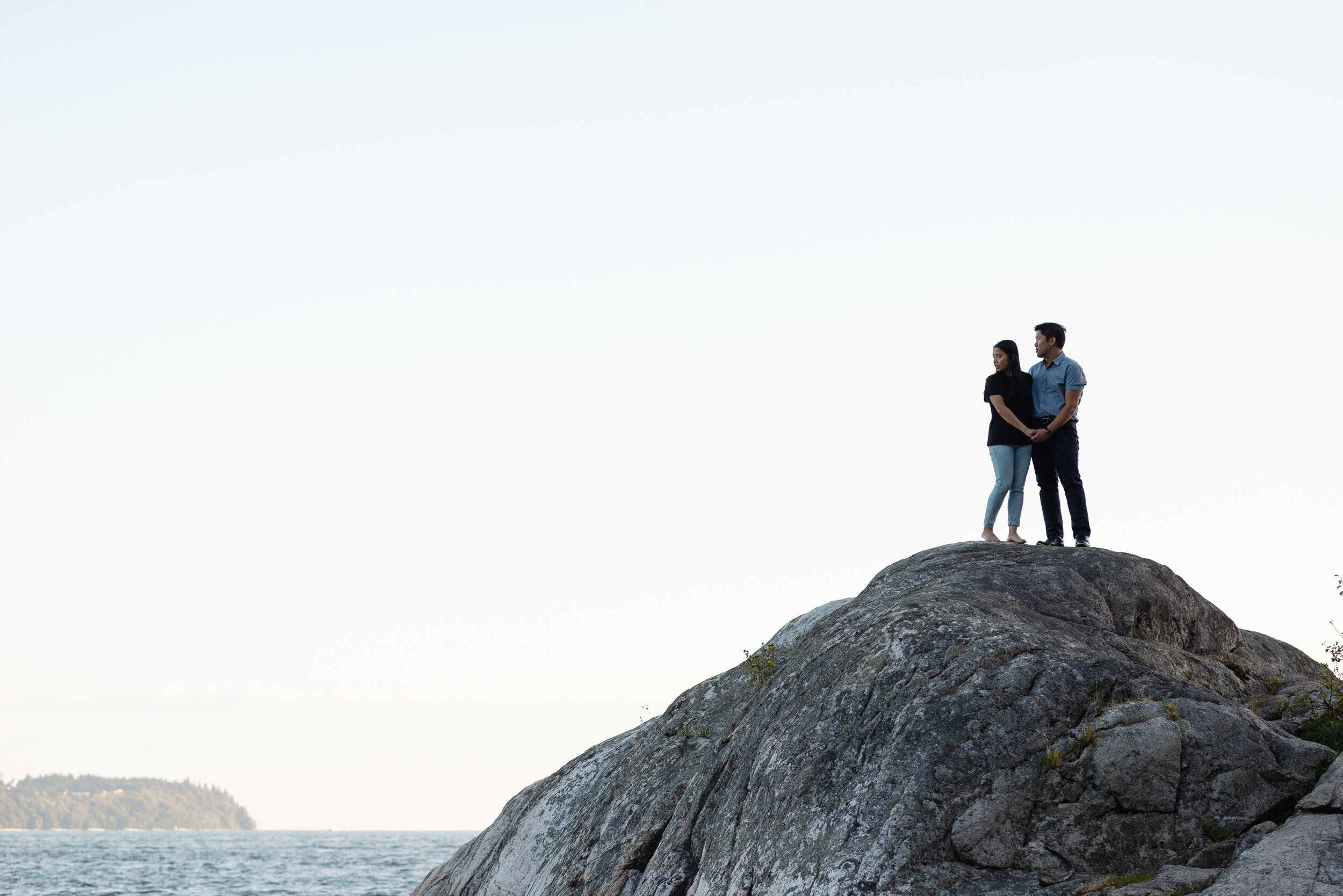 Couple stands on rock next to ocean in distance