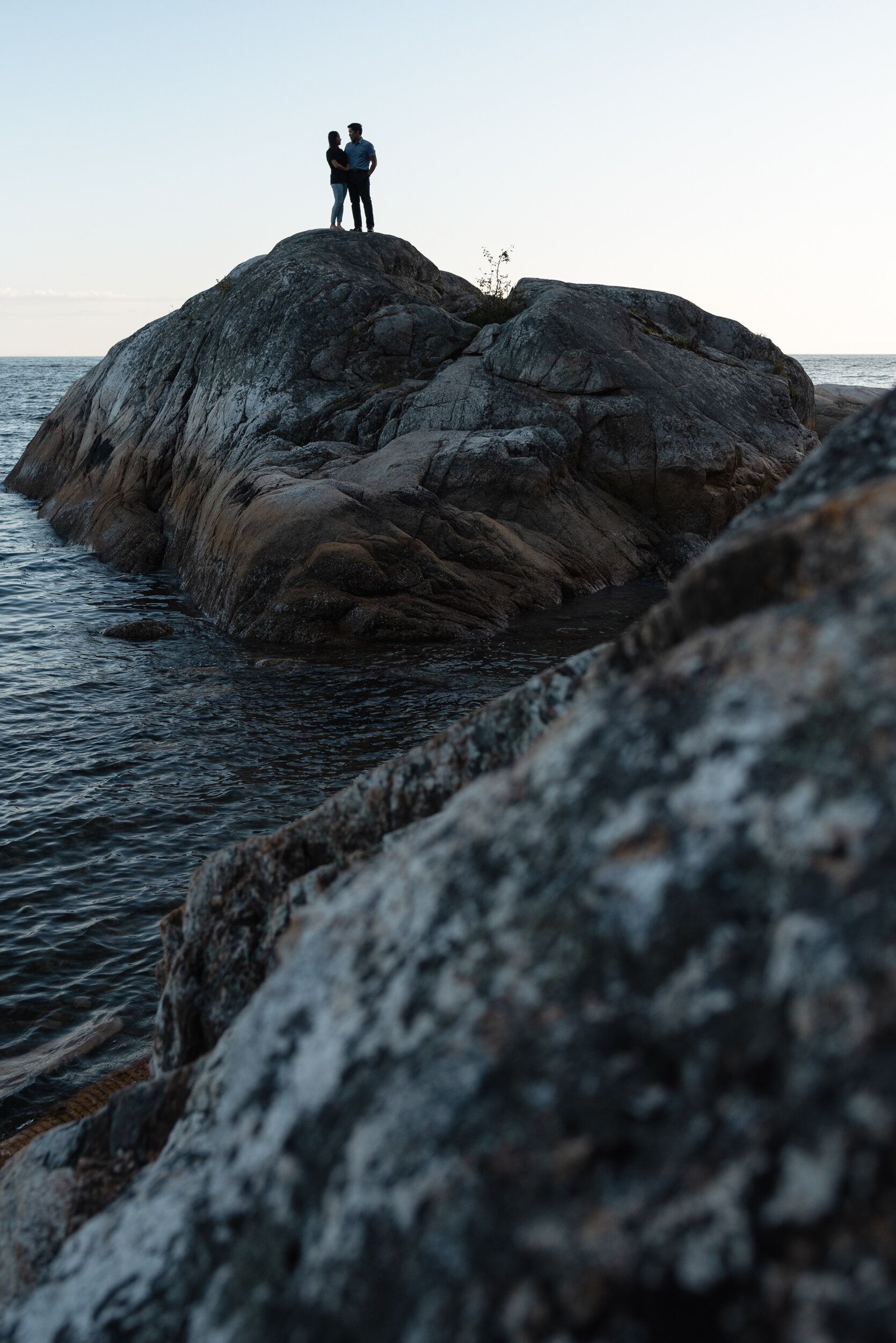 Couple stands together on rock surrounded by ocean