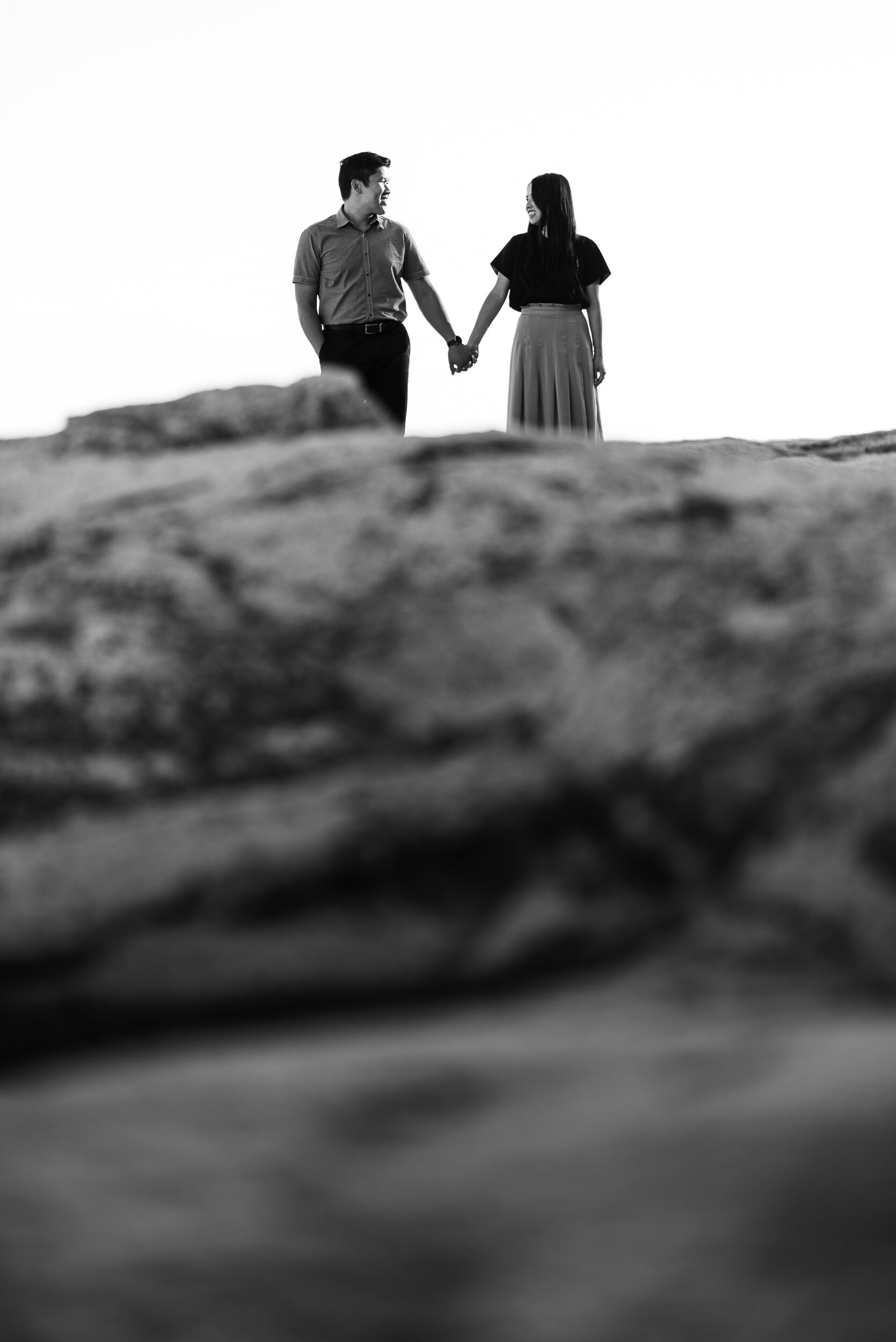 Couple holds hands on rocky shore