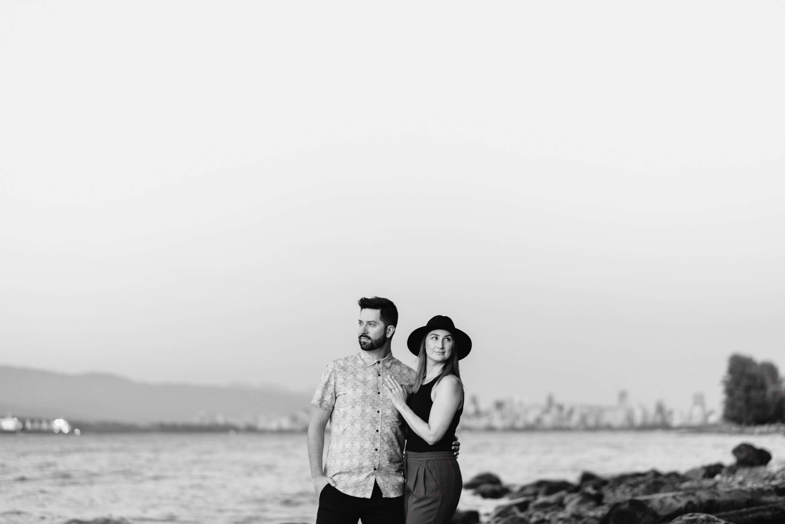 Couple standing Acadia Beach with Vancouver in background black and white