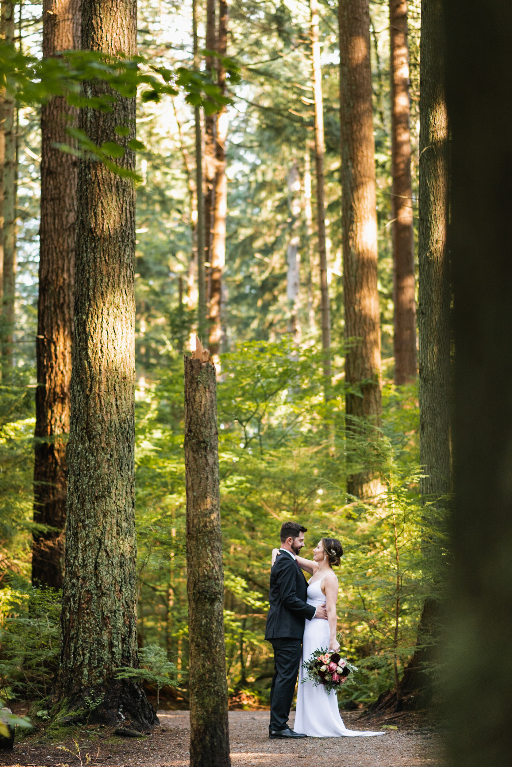 Couple stands in forest tall trees