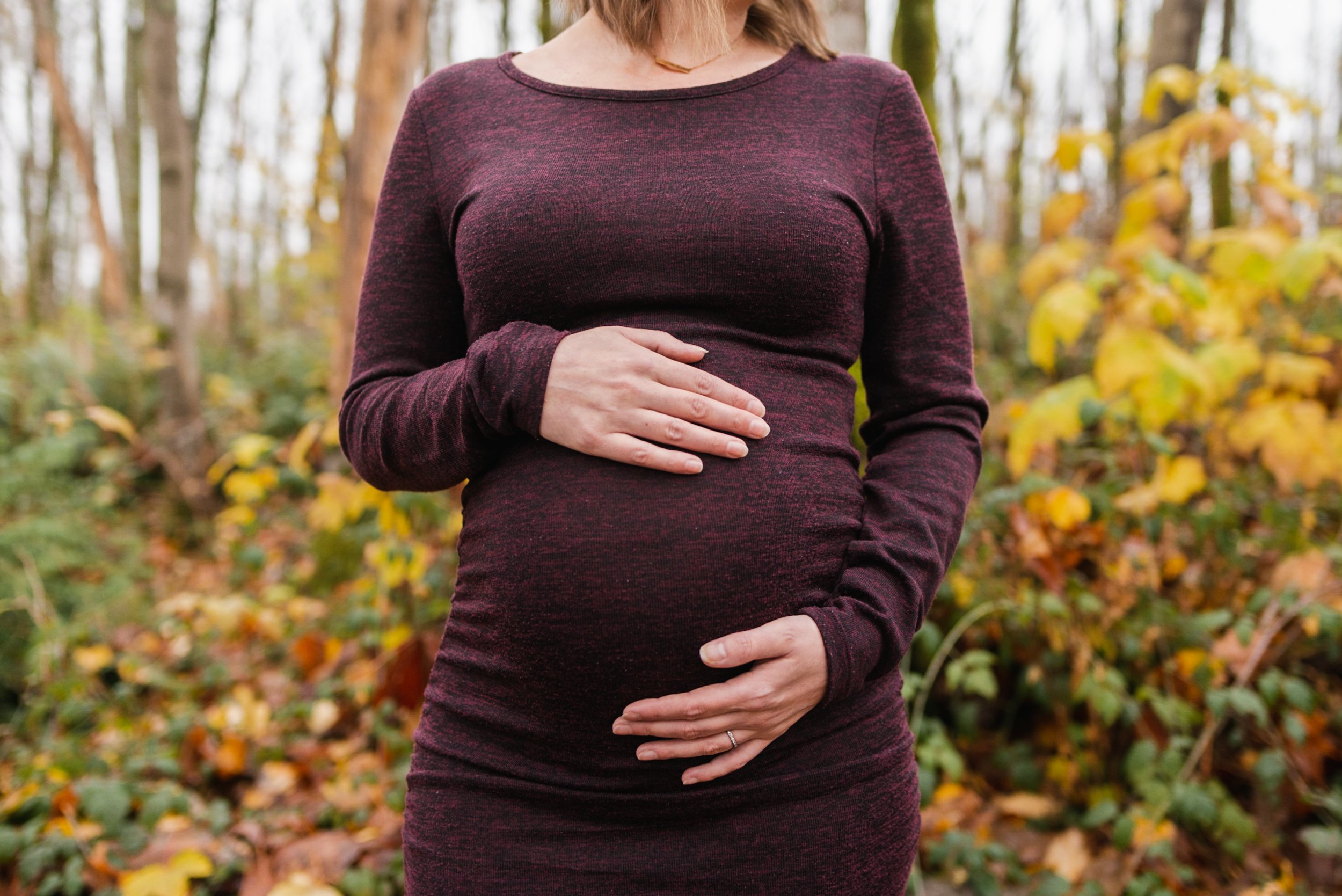Pregnant woman burgundy dress in forest holding belly