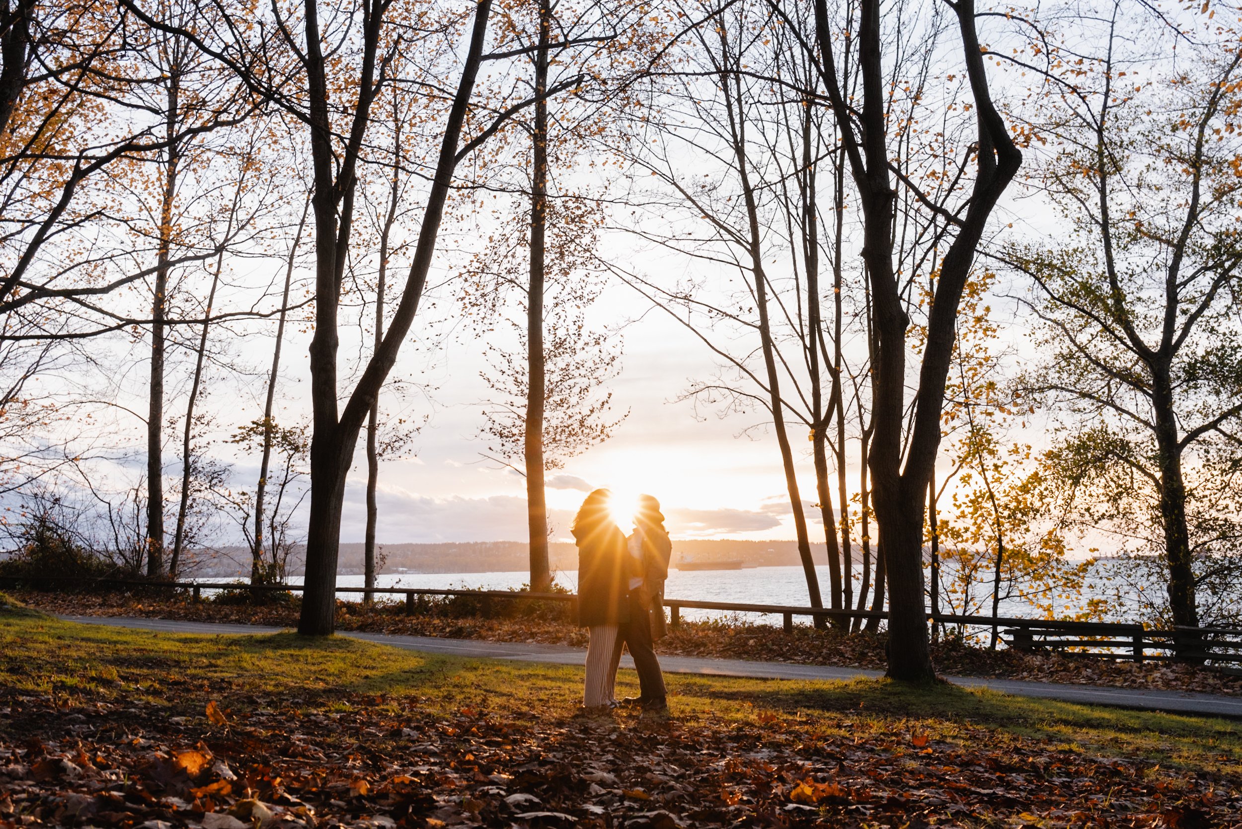 Wide shot of couple embracing in front of sunset at Stanley Park