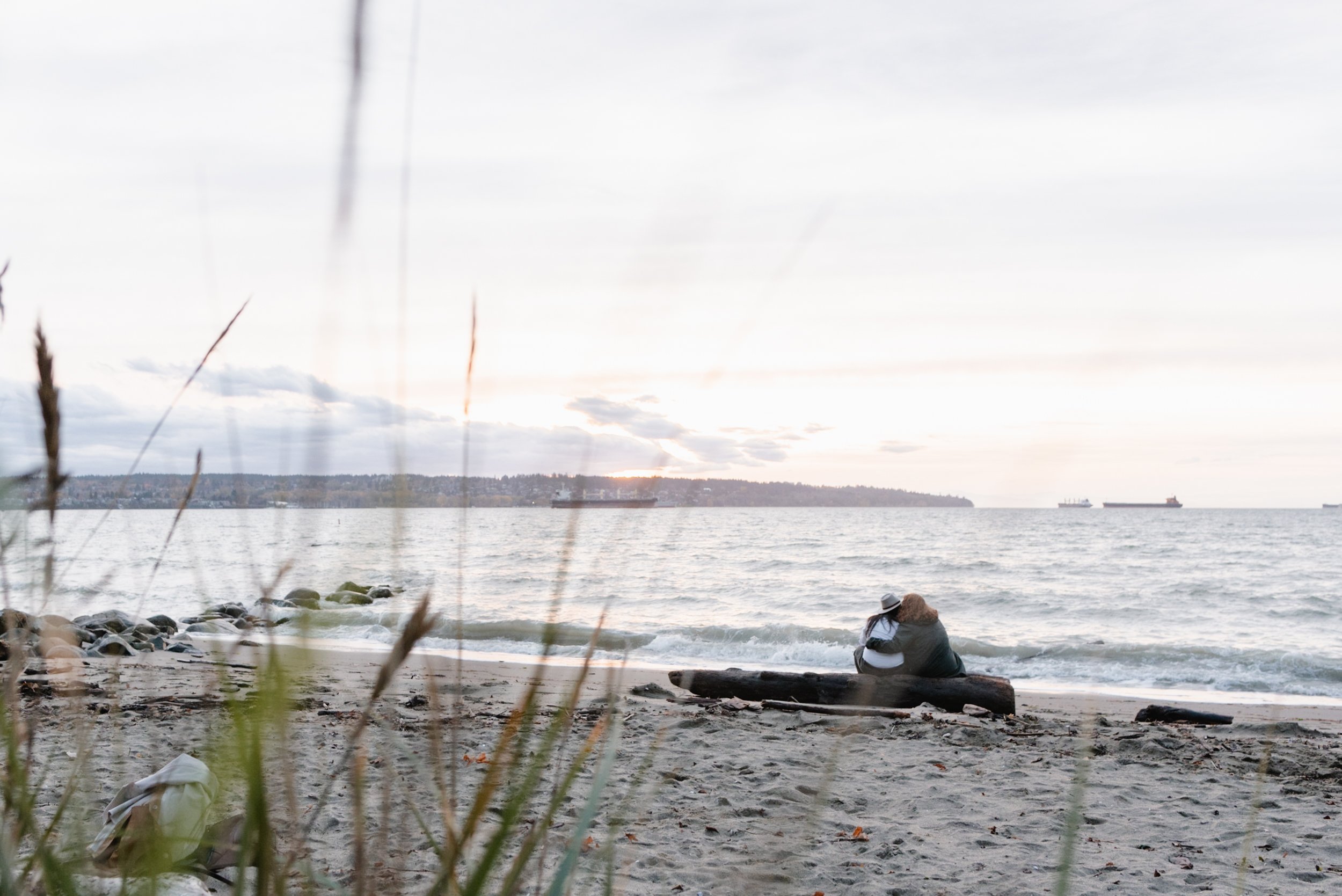 Couple snuggling while sitting on a piece of driftwood watching the sunset at Stanley Park's Second Beach