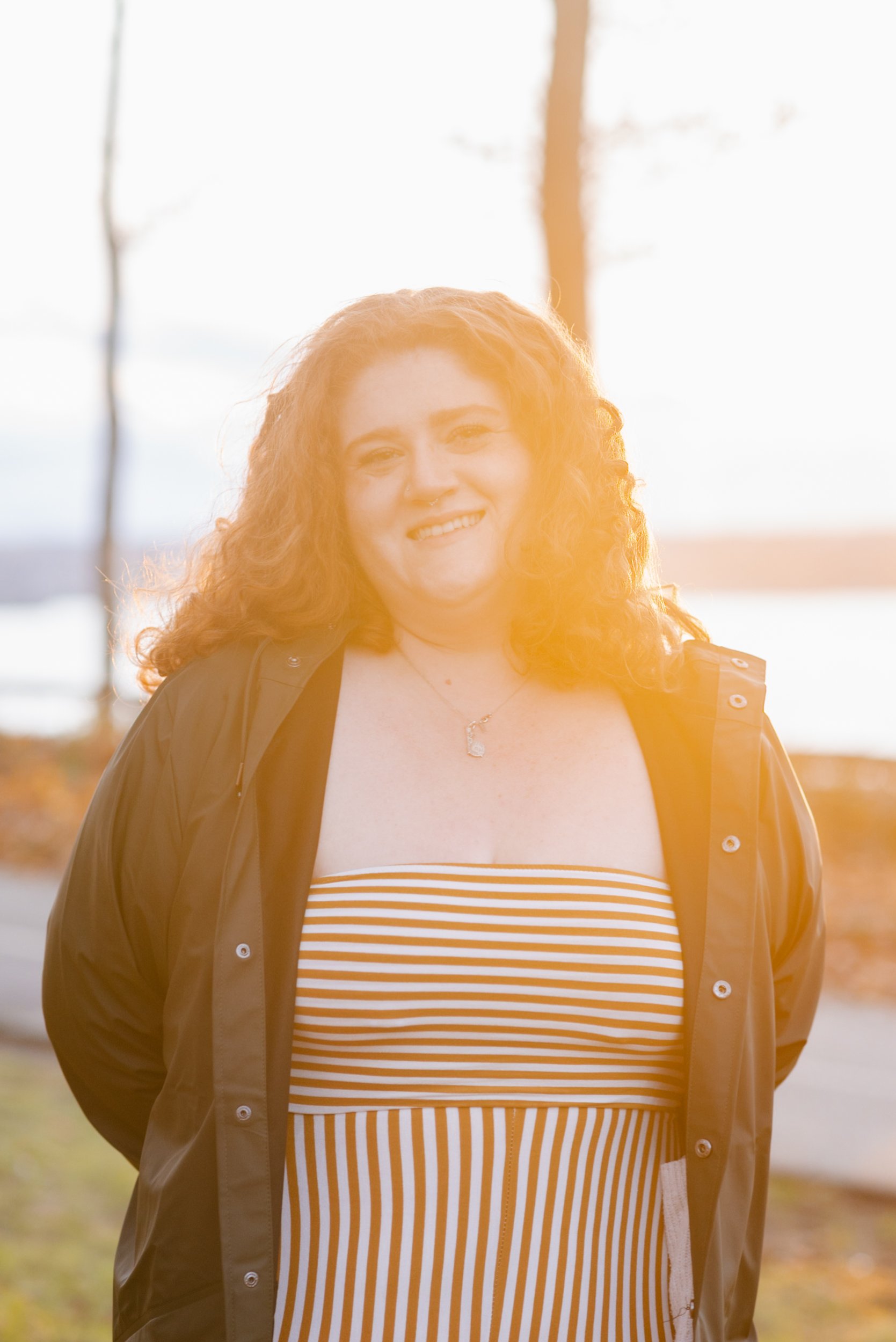 Person portrait with warm sunset glow and red curly hair smiling with sunset behind them