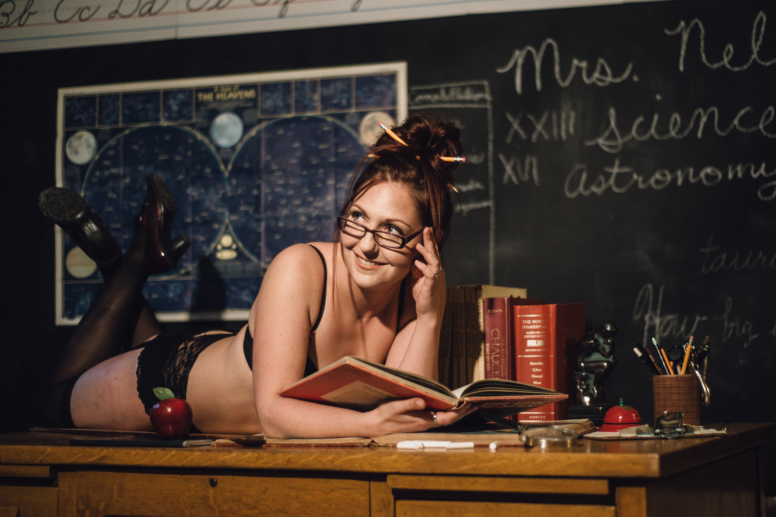  Teacher themed boudoir session, woman lays on desk, pencils in her hair, wearing glasses, science poster, reading a book. Tags: PNW Boudoir Photographer Bellevue Issaquah north bend Snoqualmie Seattle self care body image body neutrality fun photosh
