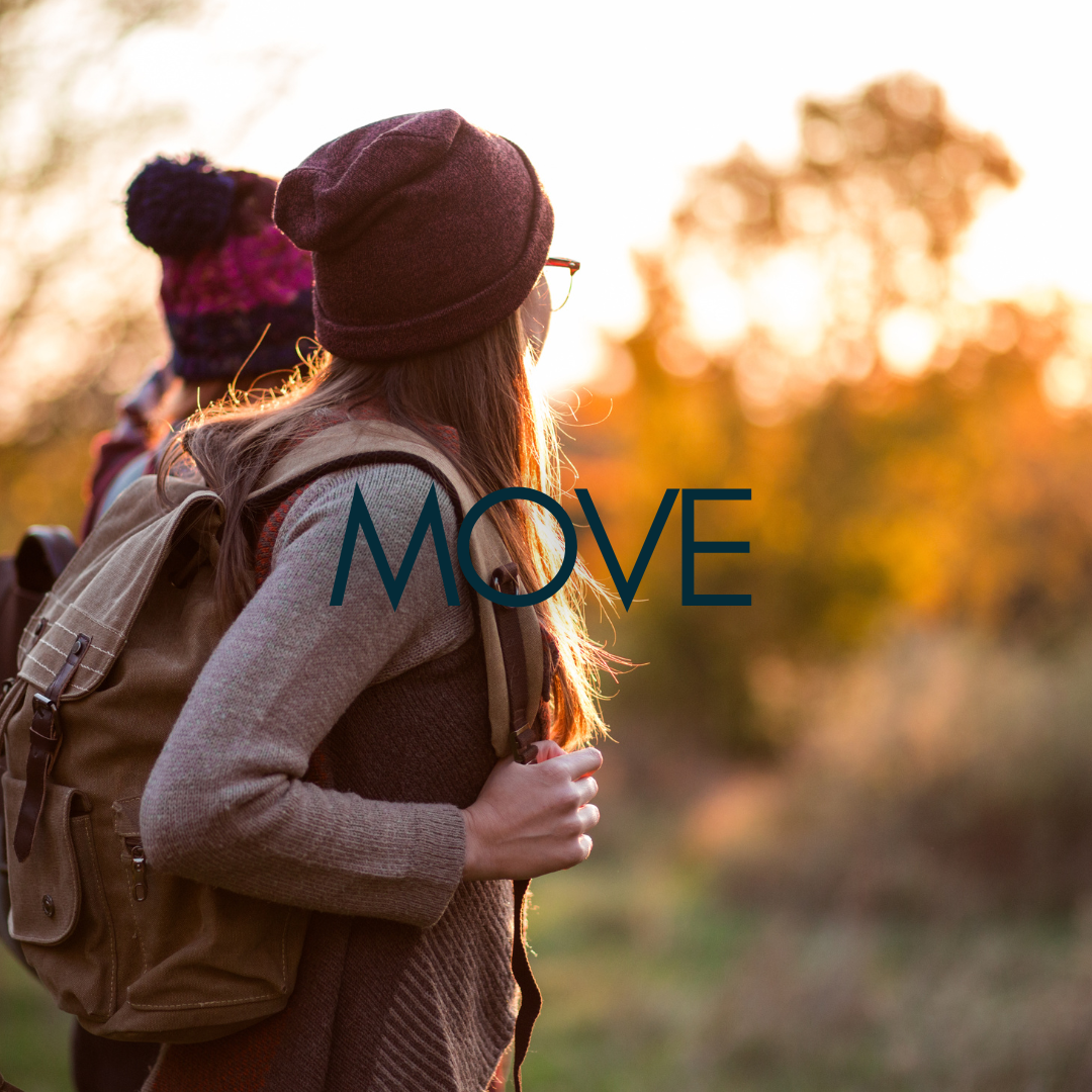 two women hike together in the fall, facing away from the camera to take in the sunset