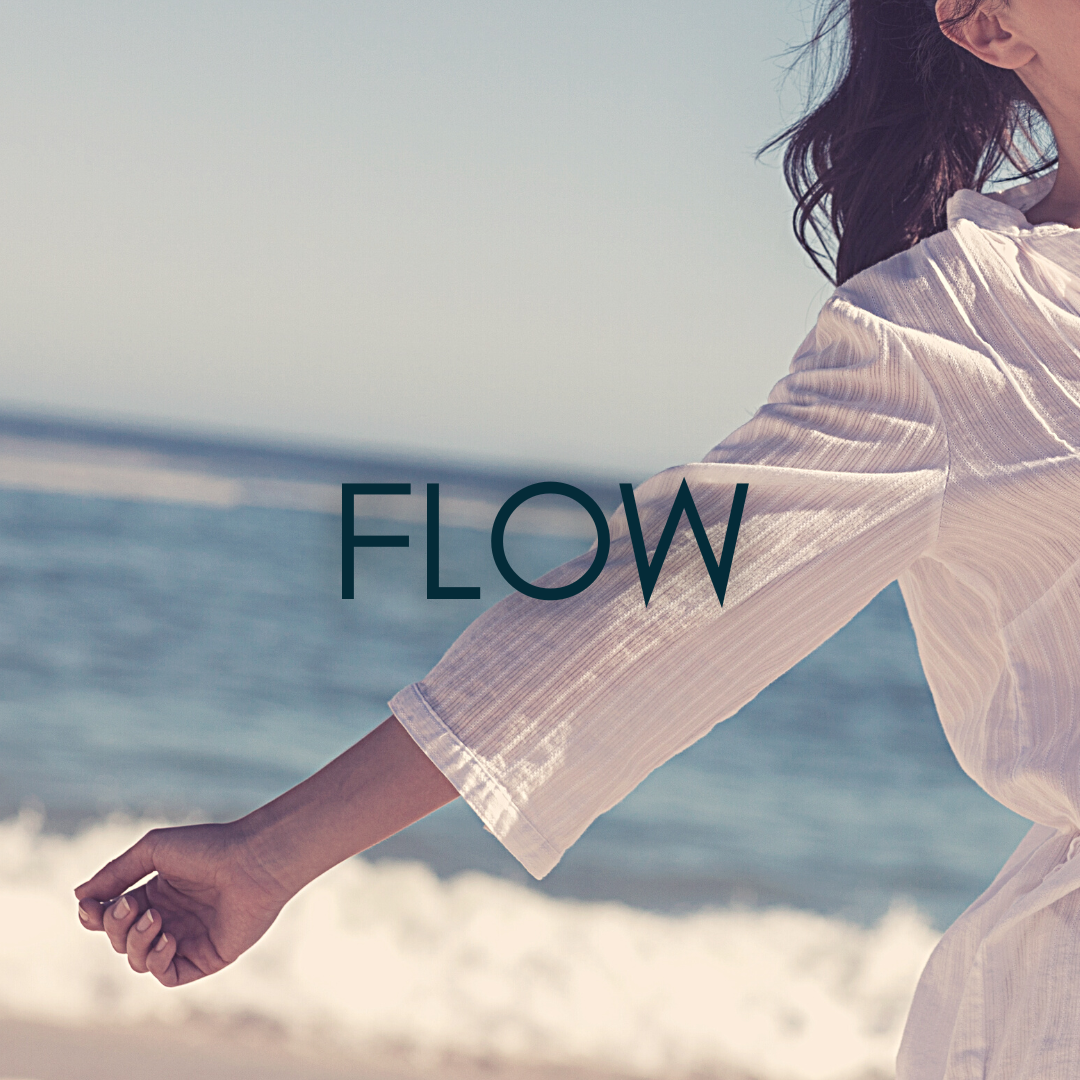 woman stands with arms out in a crisp white shirt enjoying the ocean we see with waves crashing peacefully behind her