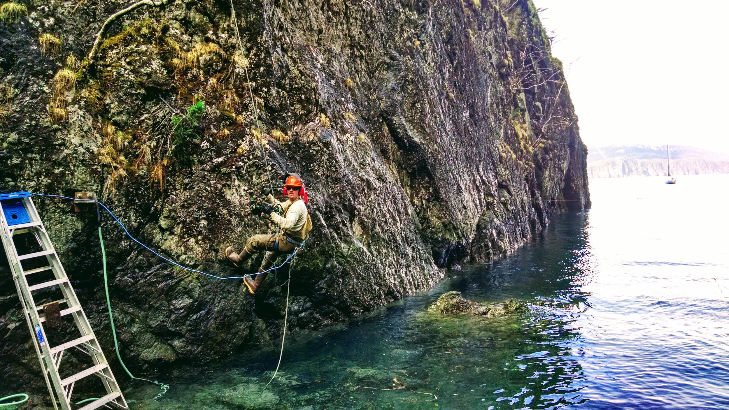  This is one of the very first photos from building Shearwater Cove featuring our dear friend Jesse repelling off the cliff with a hammer drill to drill holes for the steel supports that would be anchored into the cliff wall to carry our dock beams. 