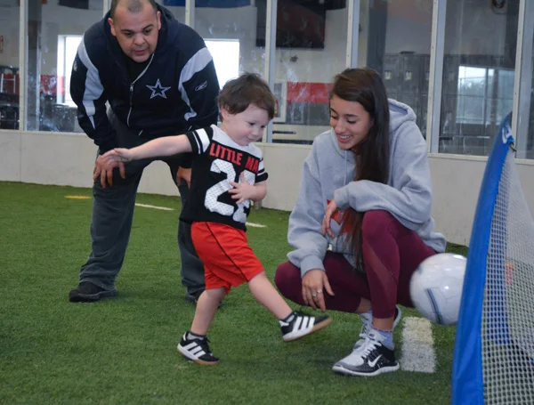 Parent and Coach Help Boy Shoot Ball Into Goal