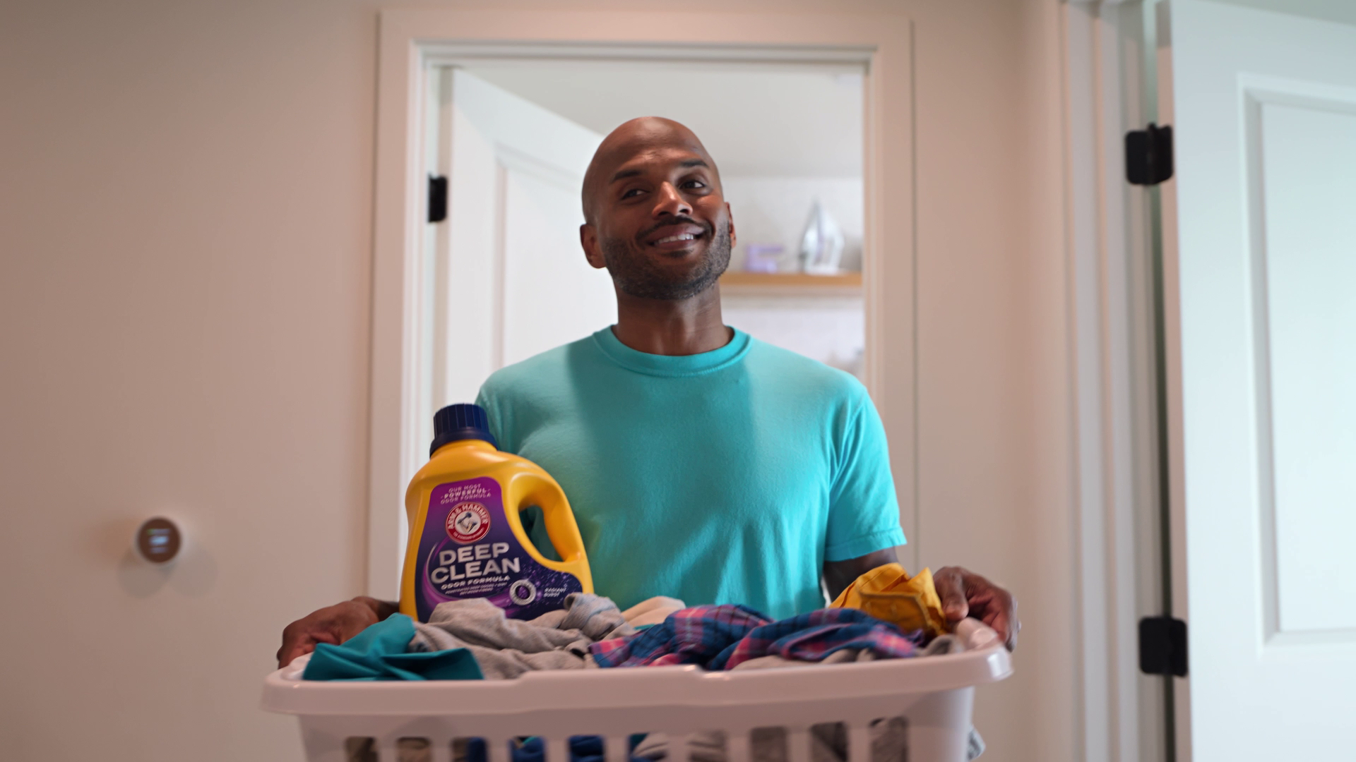 Still from advertising spot. Happy man carrying basket filled with dirty laundry and a bottle of Arm & Hammer Deep Clean