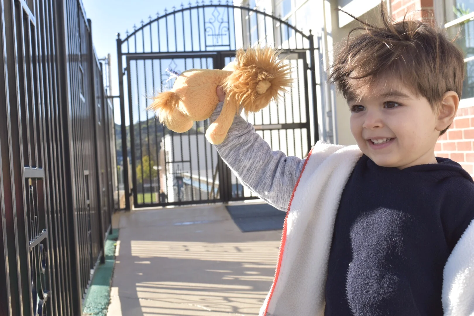 Leo smiling and holding toy lion, excited for his first day of preschool.