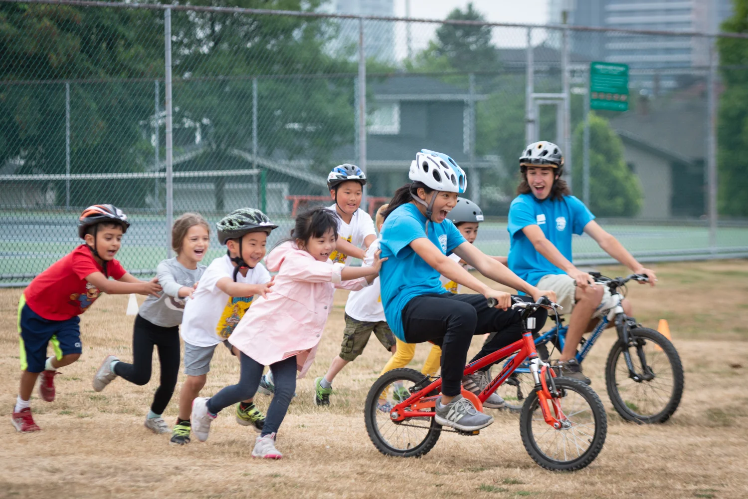 Children pushing Pedalheads instructors on bicycles, laughing as they race during this fun camp event.