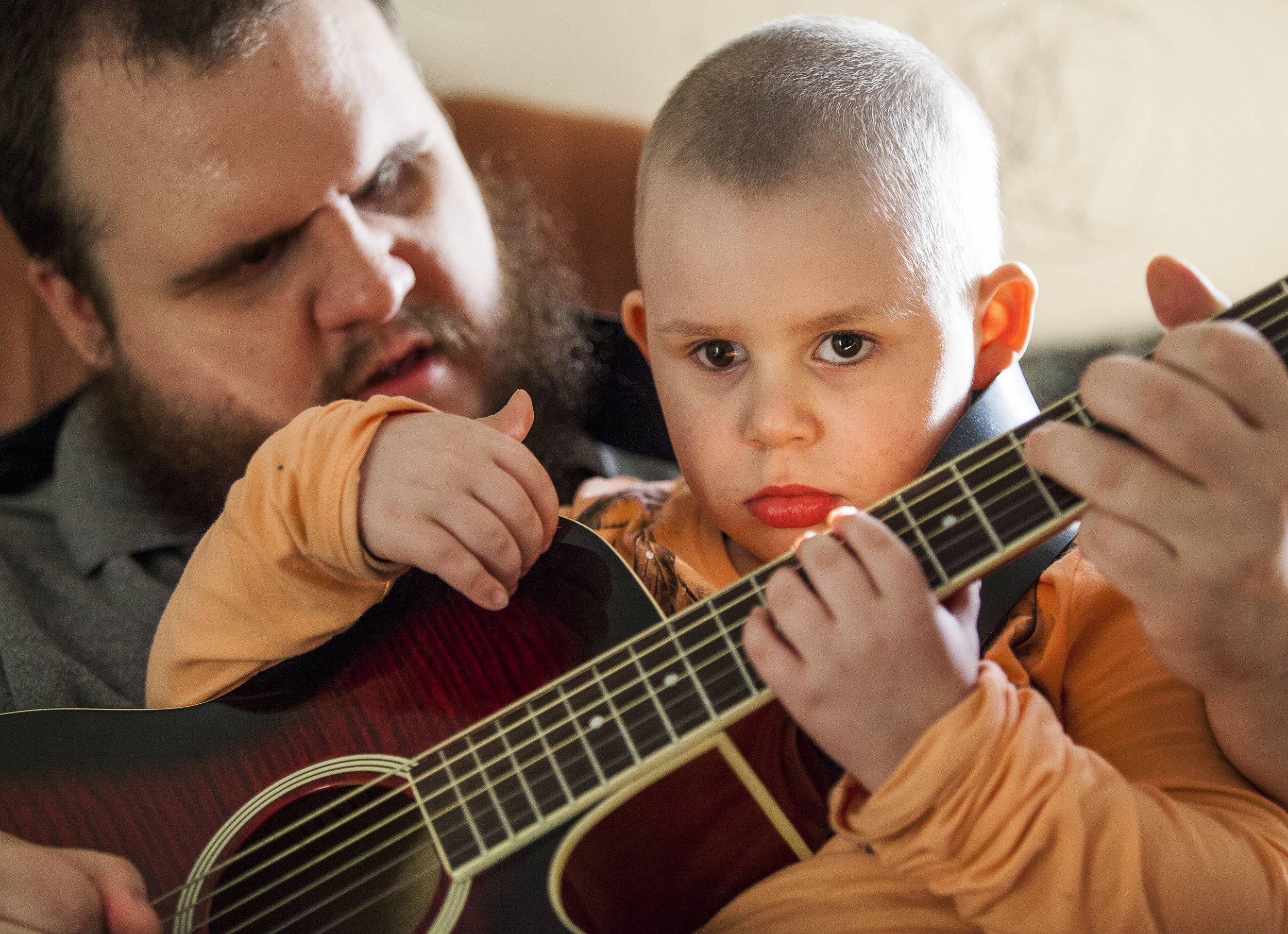 Sean Jordan teaches Cassie how to strum the guitar in their home. Sean passed down his love of music to Cassie who is learning how to play piano and guitar. Sean had both of his eyes removed 14 years ago but continues to be a musician of multiple instruments including drums, guitar and piano.