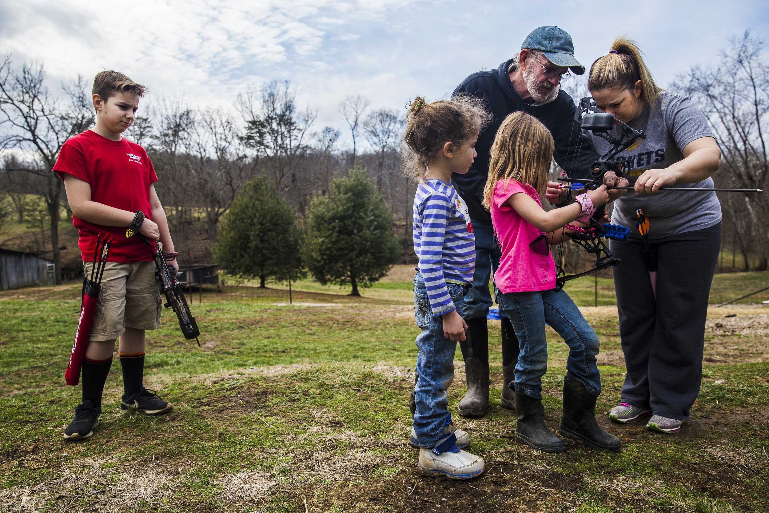 Luke Jonas waits to shoot his bow while his mother and grandfather coach his sister Emily on how to hold her bow.