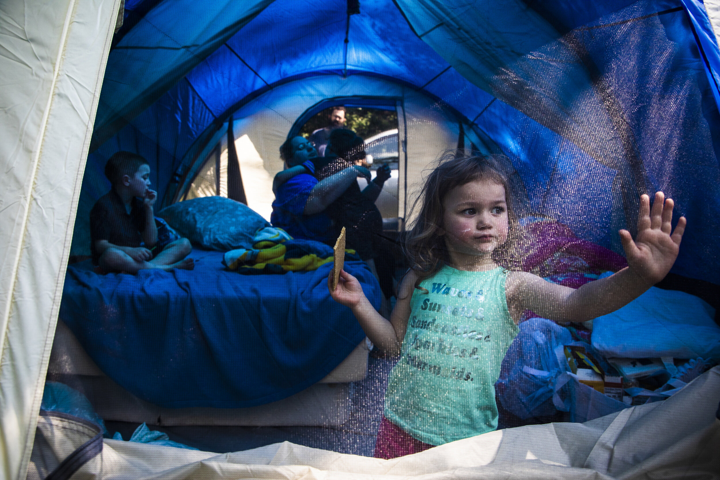 Laya Lupien eats a graham cracker and rests her hand on the door of her family's tent while trying to escape the summer heat with her brother Dylan, left, mother Mariah, brother Evan and father Patric