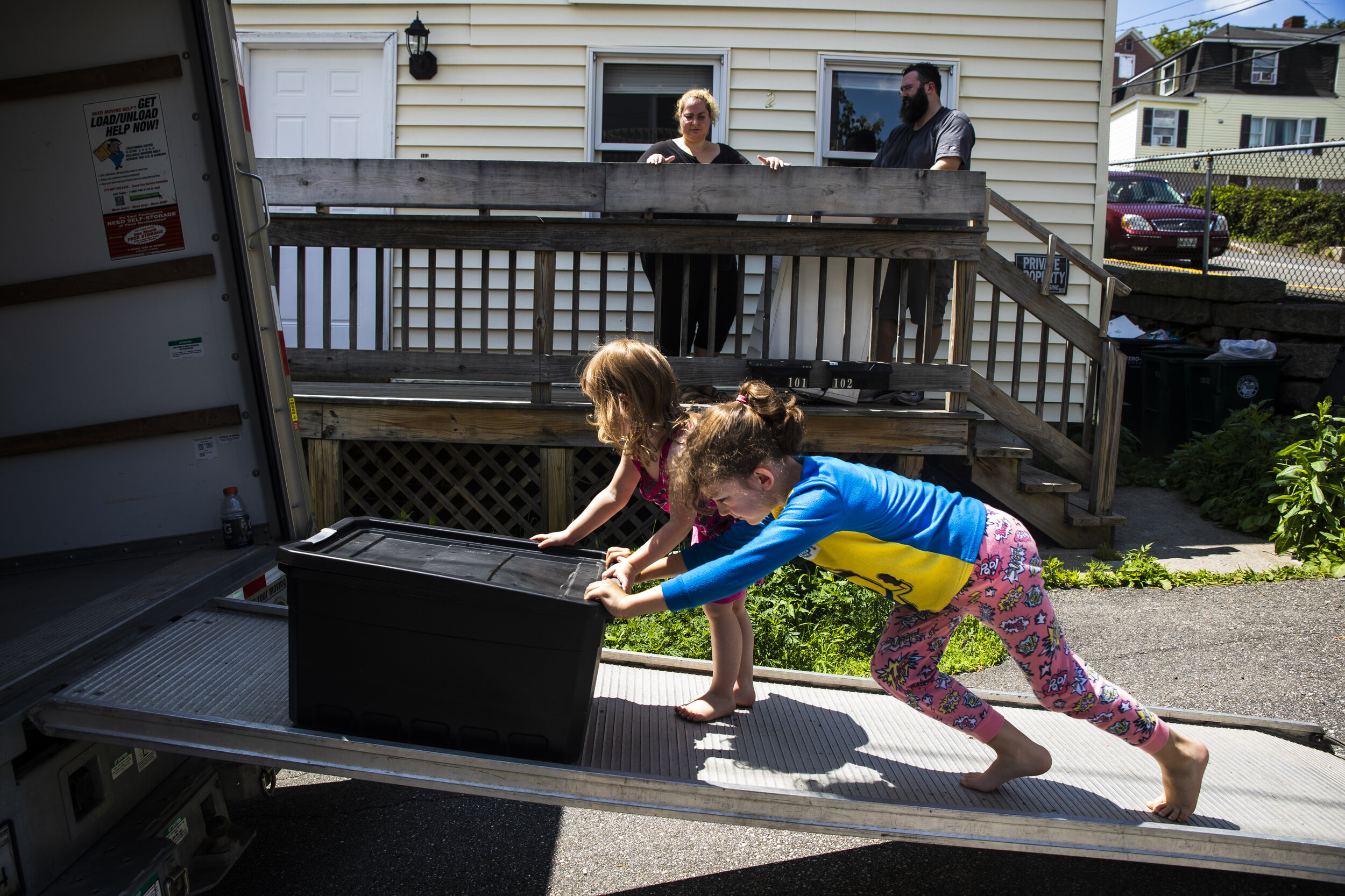 Siblings Laya, left and Evan Lupien push a tote up the ramp of the U-Haul while their parents, Mariah LeMieux-Lupien and Patrick Lupien, watch from the porch of their apartment. "More, more, more!" ye