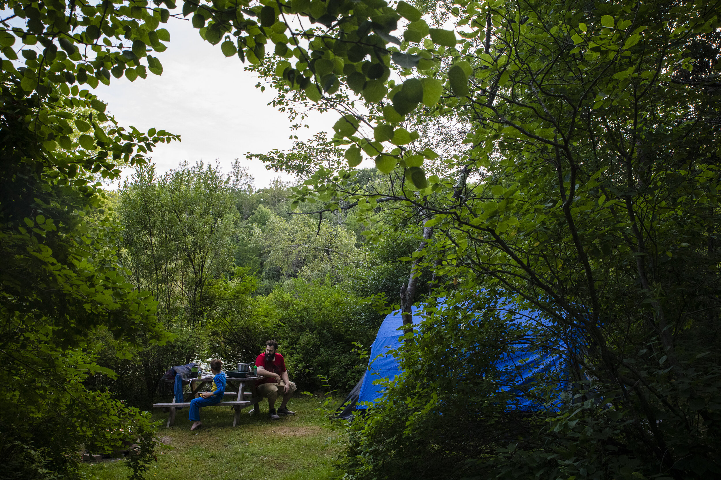 Patrick Lupien sits with his son Evan at their campsite while siblings Laya and Dylan watch movies in the van.  With the children's special needs, Mariah and Patrick have found it difficult to keep an