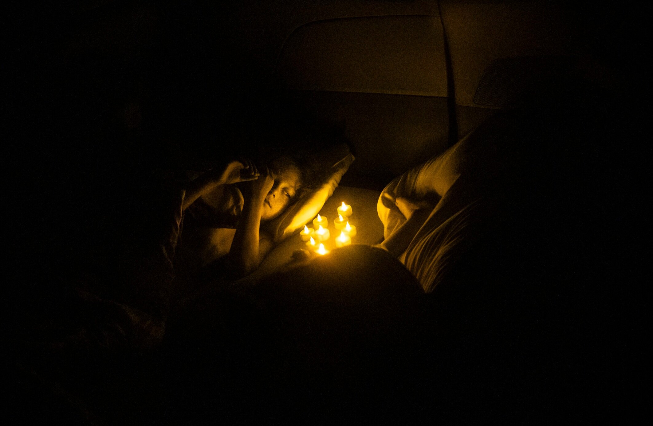 Evan Lupien watches as battery operated tea lights flicker while he drifts off to sleep. Curled up next to his two siblings, the children spend their first night sleeping in the family's van at a camp
