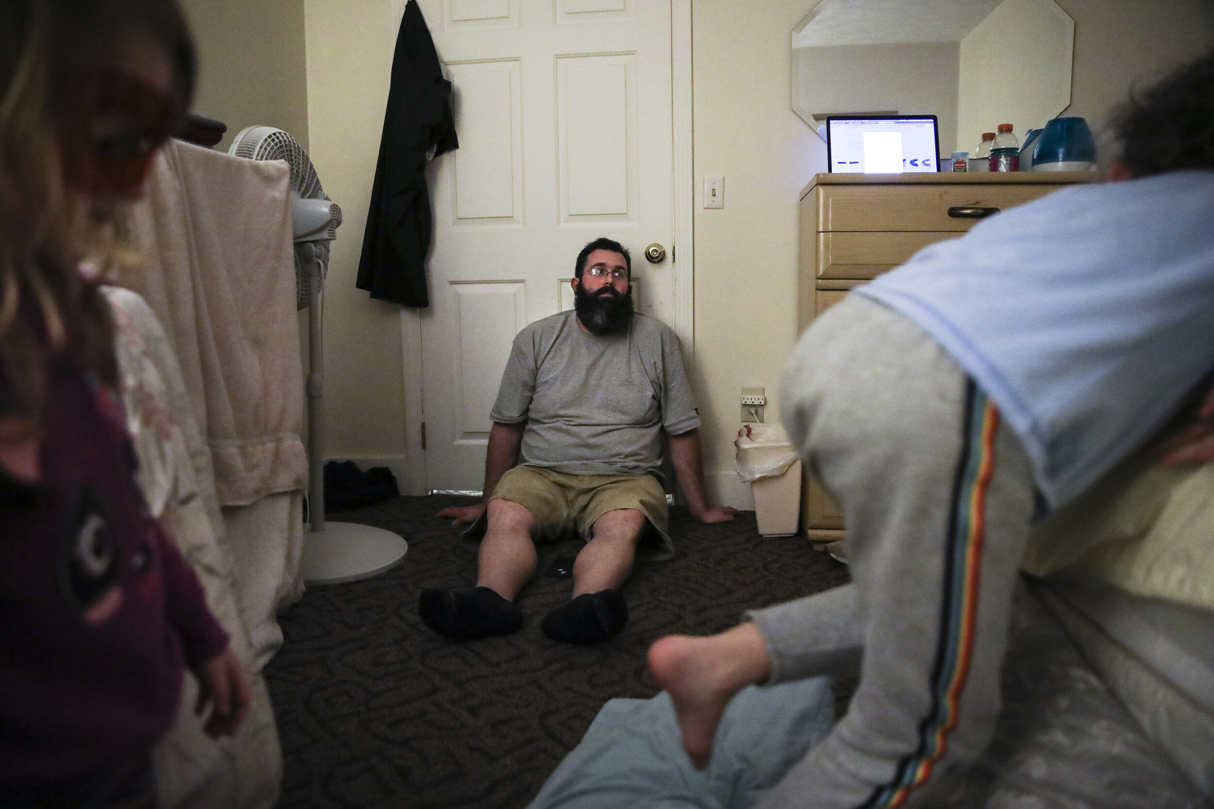 Exhausted, Patrick Lupien leans against the bedroom door while his daughter Laya, left, and son Evan jump back and forth on the bed. The family has been at Seacoast Family Promise, a shelter program i