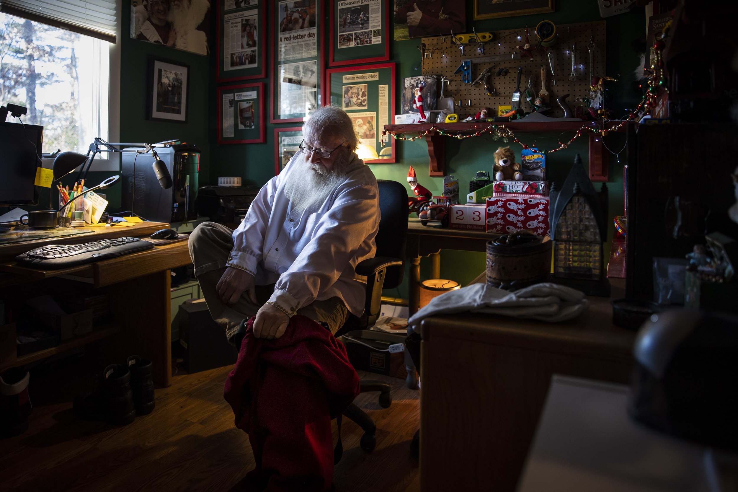  Bob Jordan puts on his Santa suit while in the office of his Framingham, Mass. home on December 2, 2022. He has the office decorated like Santa’s workshop; tools lining the walls and carefully wrapped Christmas presents rest behind his chair. It cam