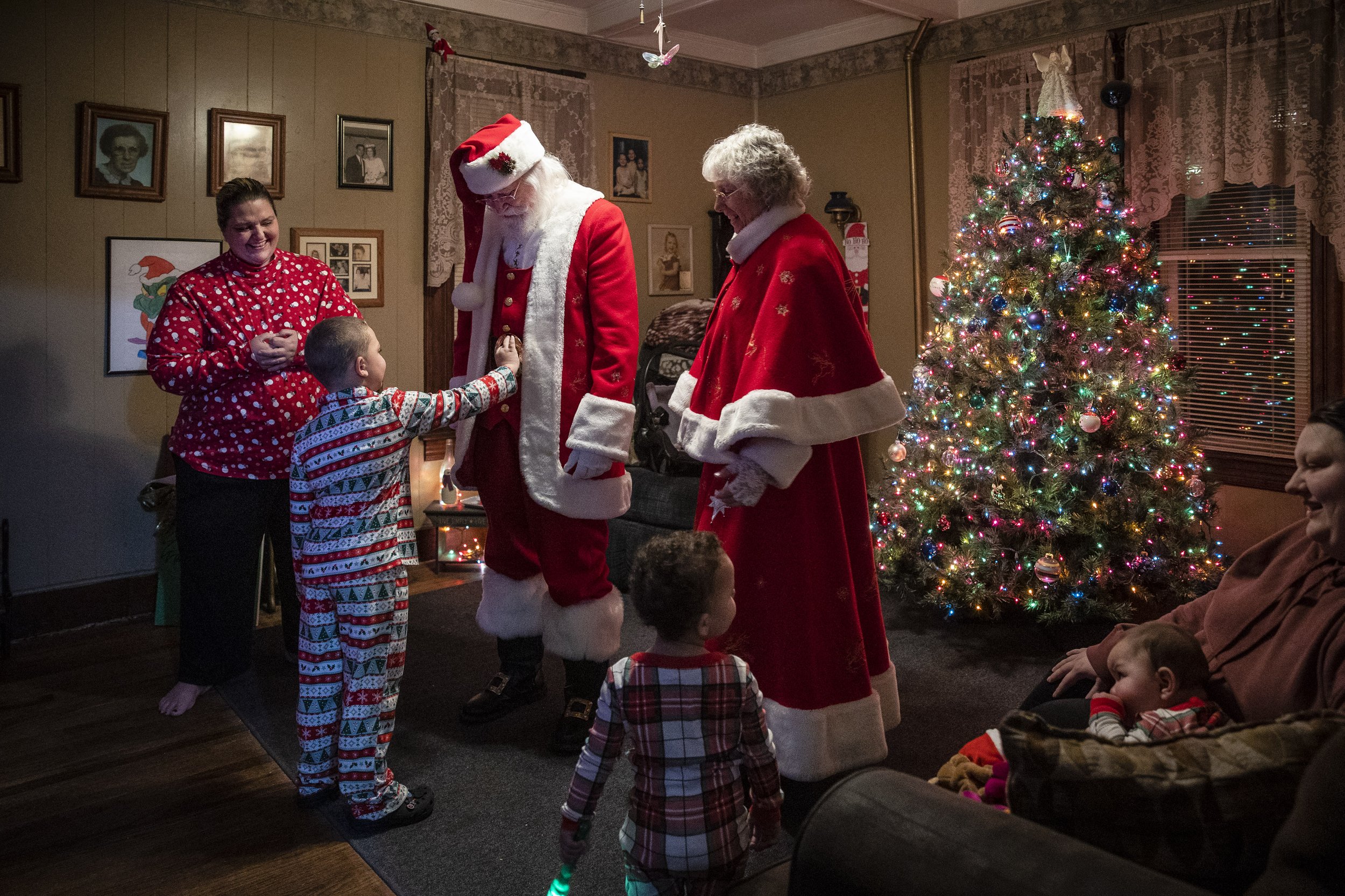  Daunte Russo places his hand on the belt of Santa Claus, portrayed by Lenny Stratton, during a home visit with Mrs. Claus, portrayed by Becki Stratton, at the Russo’s home on December 3, 2022. It’s their fifth stop today as Mr. and Mrs. Claus, with 