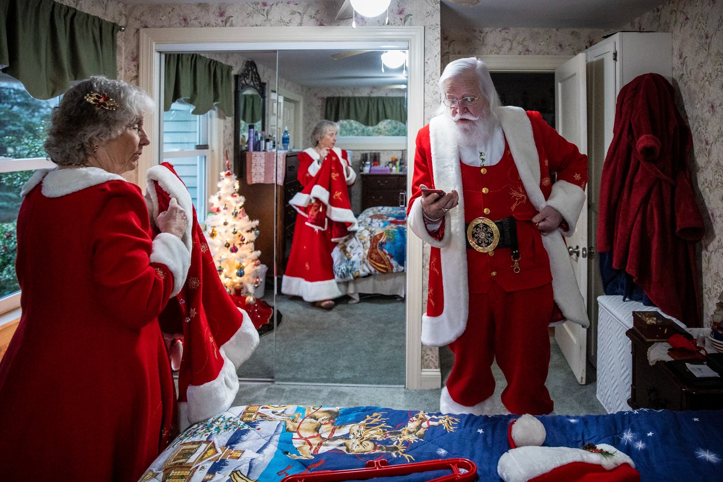  Becki and Lenny Stratton get dressed for a full day of performing as Mr. and Mrs. Claus on December 3, 2022. A Christmas blanket adorns their bed and a decorated tree is in each room of their Shelburne, Mass. home. Becki has a vast walk-in closet, m