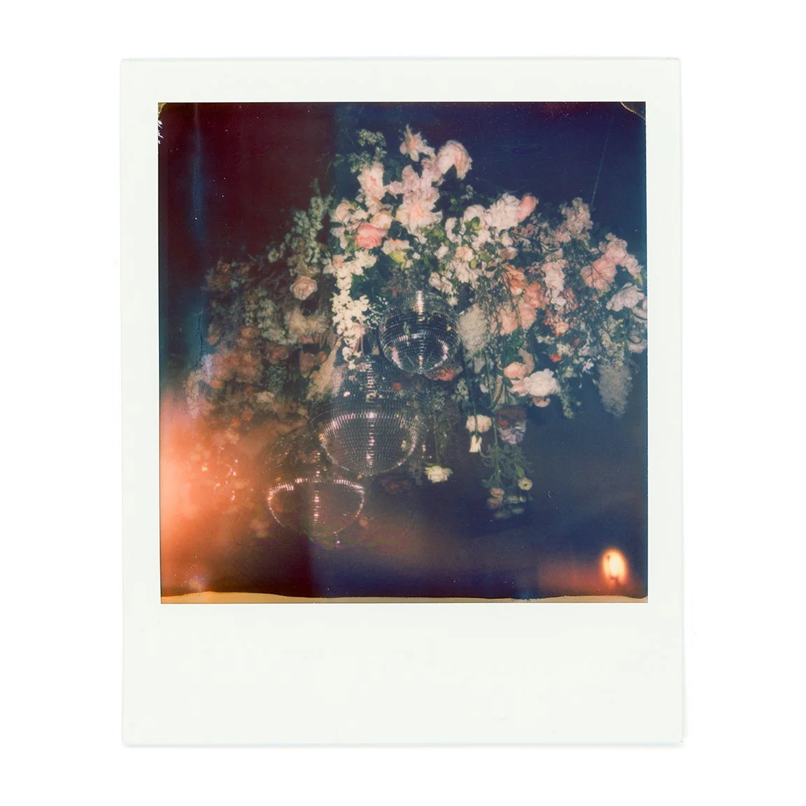 Polaroid photo of a flower arrangement with pink and white flowers and disco balls hanging in the center