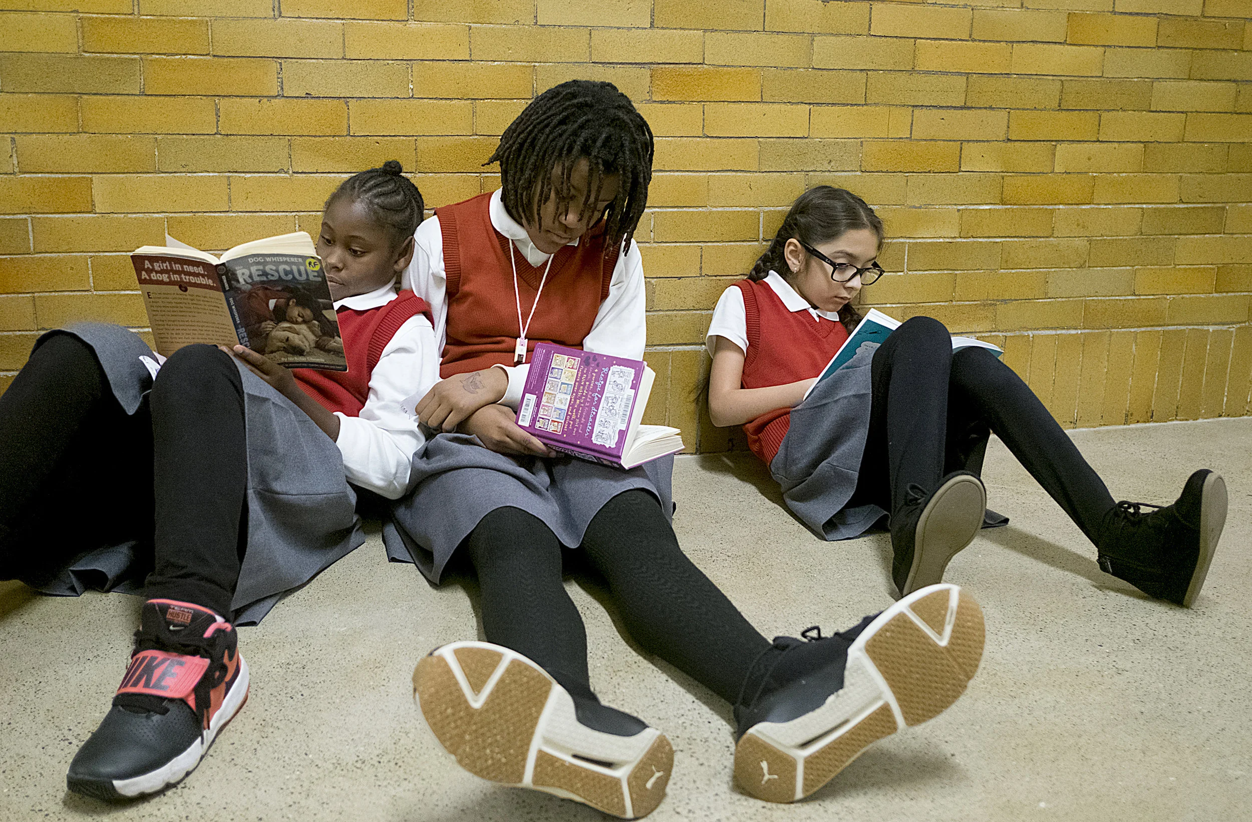 Nancia Buchanan leans into Patience Epps while they read quietly in a hallway with Shelly Marquez Sanchez at Ascension School.