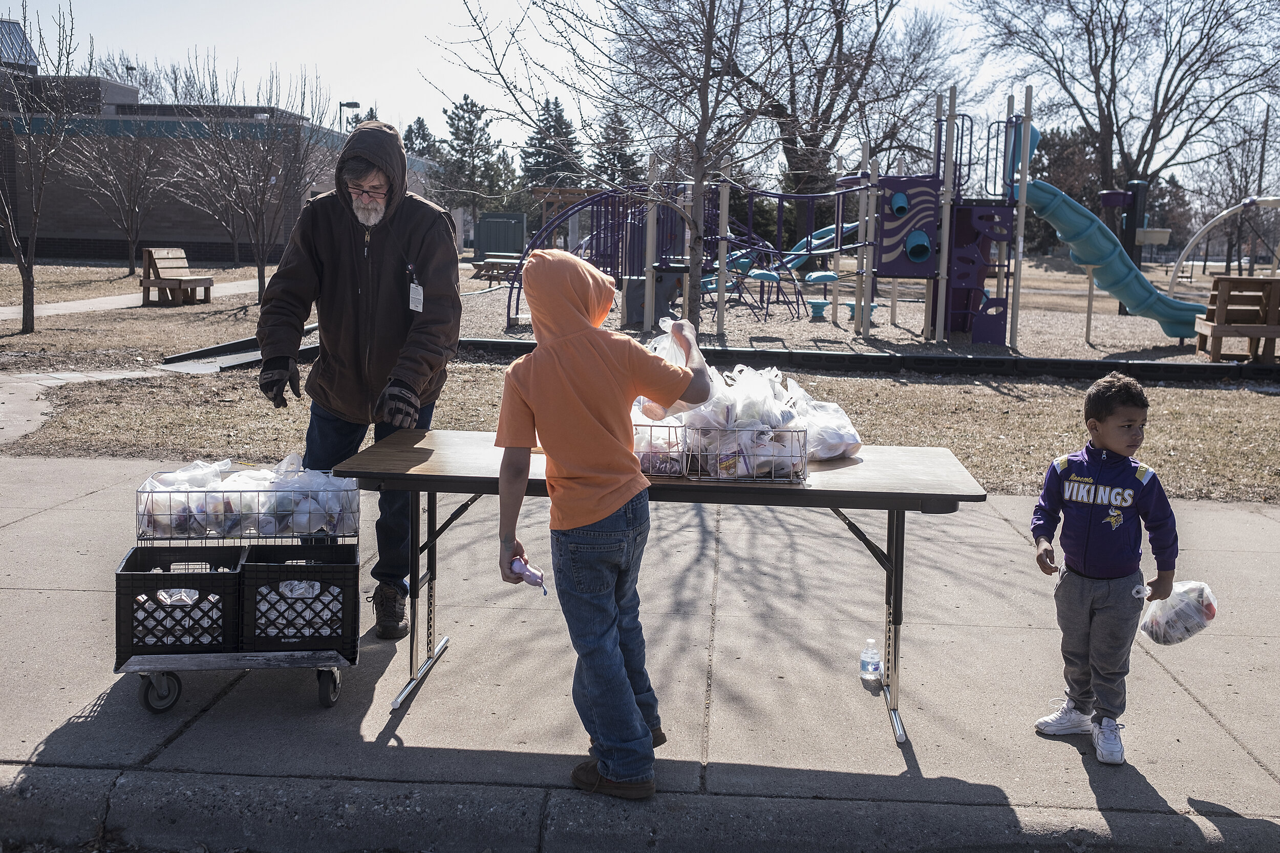  Bus driver Steve Towle reaches for milk while brothers Durell and DeRoyal Perry, right, pick up food bags outside Jenny Lind Elementary School. With classrooms closed, Minneapolis Public Schools continued free student meals.  