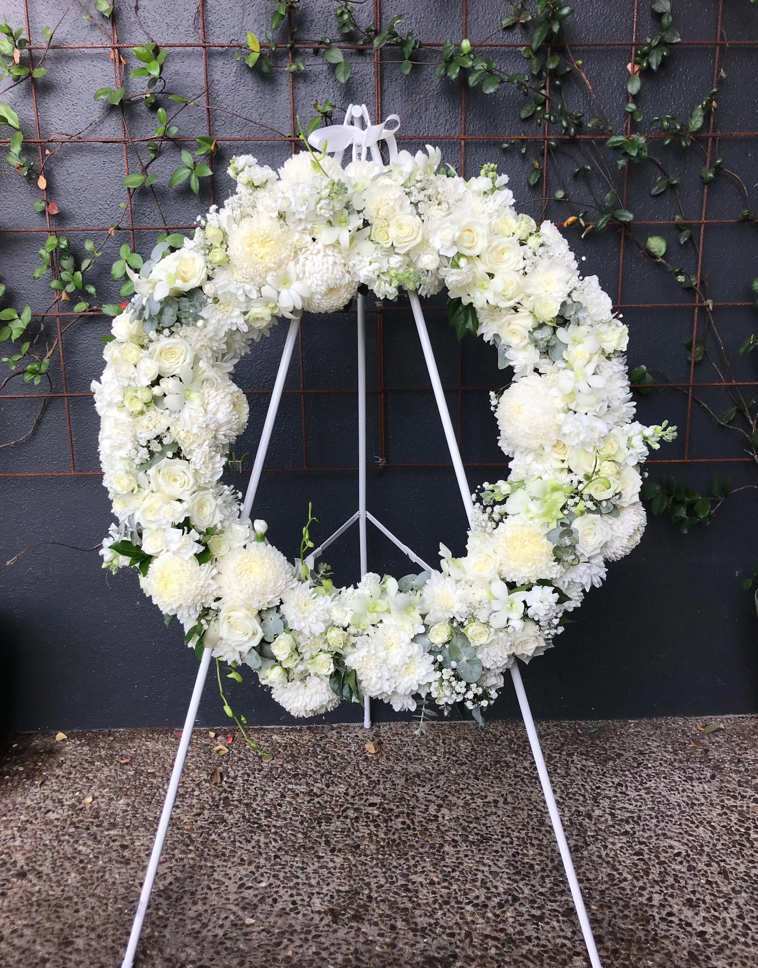 Beautiful sympathy wreath floral arrangement created with seasonal white flowers and accents of grey foliage.