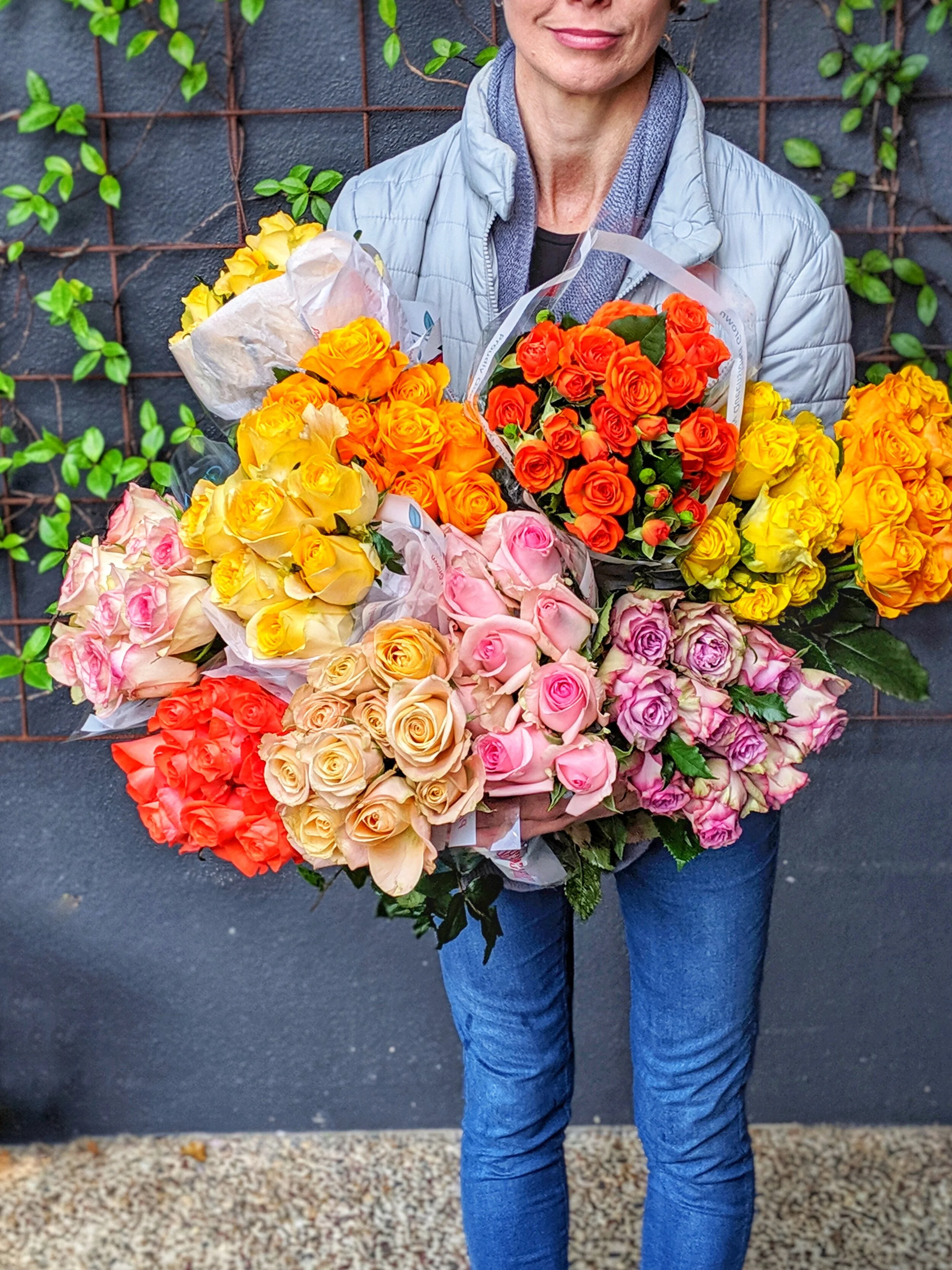 Standing person holding an adundance of fresh, locally grown long stemmed roses in a variety of bright colours.