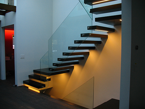 The completed stair with wood-clad steel treads and glass panel rails. LED lights illuminate the underside of the stair with a warm glow that complements the cooler daylighting coming from the skylight above. Image: Mark English Architects