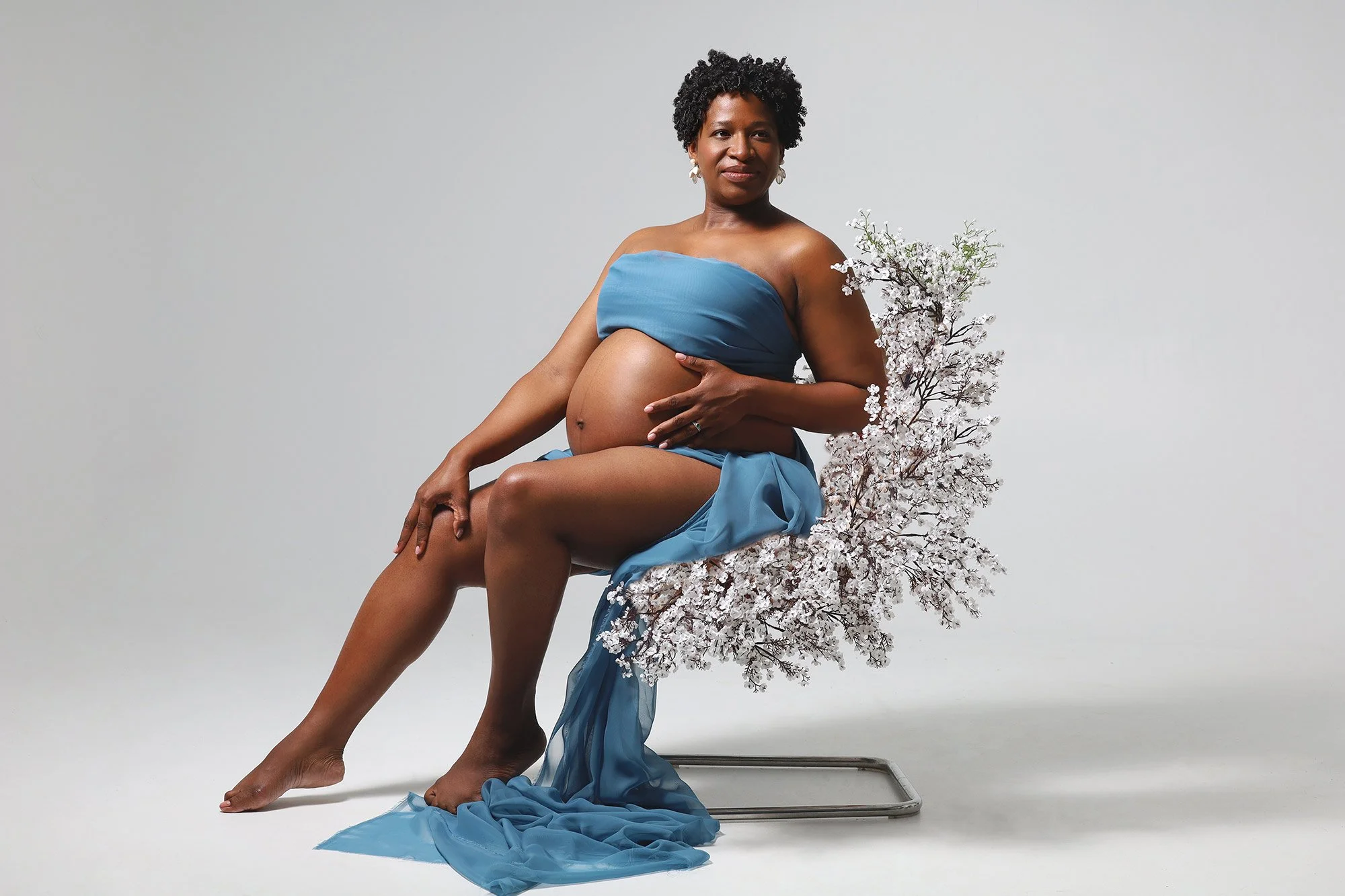 pregnant woman sitting on a chair with florals posing  in new Rochelle maternity studio