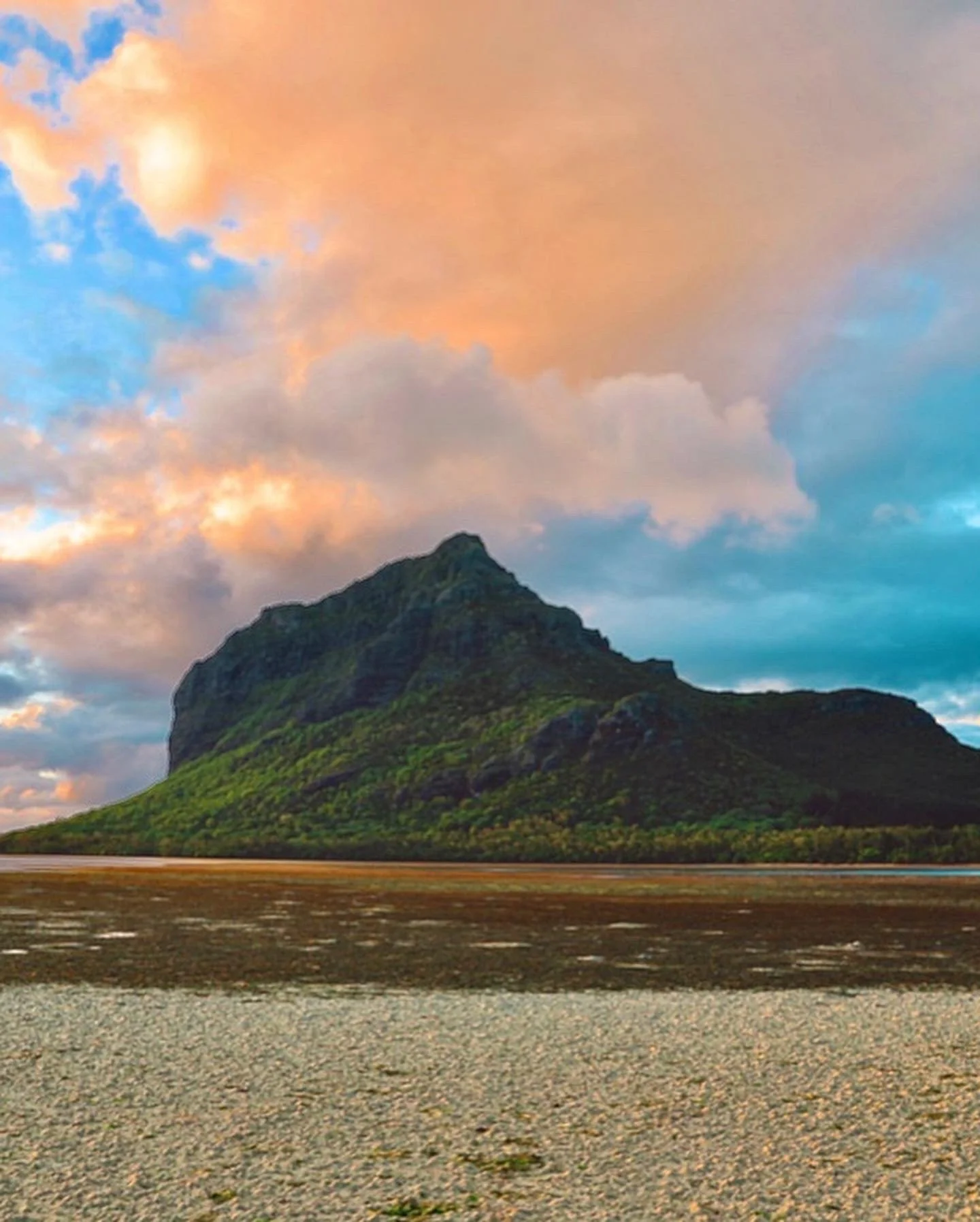Blue and Pink Sunset sky over Le Morne Mountain in Mauritius. Green trees and rocky sand beach.