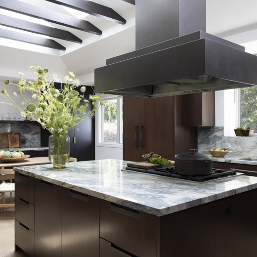 Photo of kitchen island cooktop, dark wood cabinets, and a large stainless steel cooktop hood.