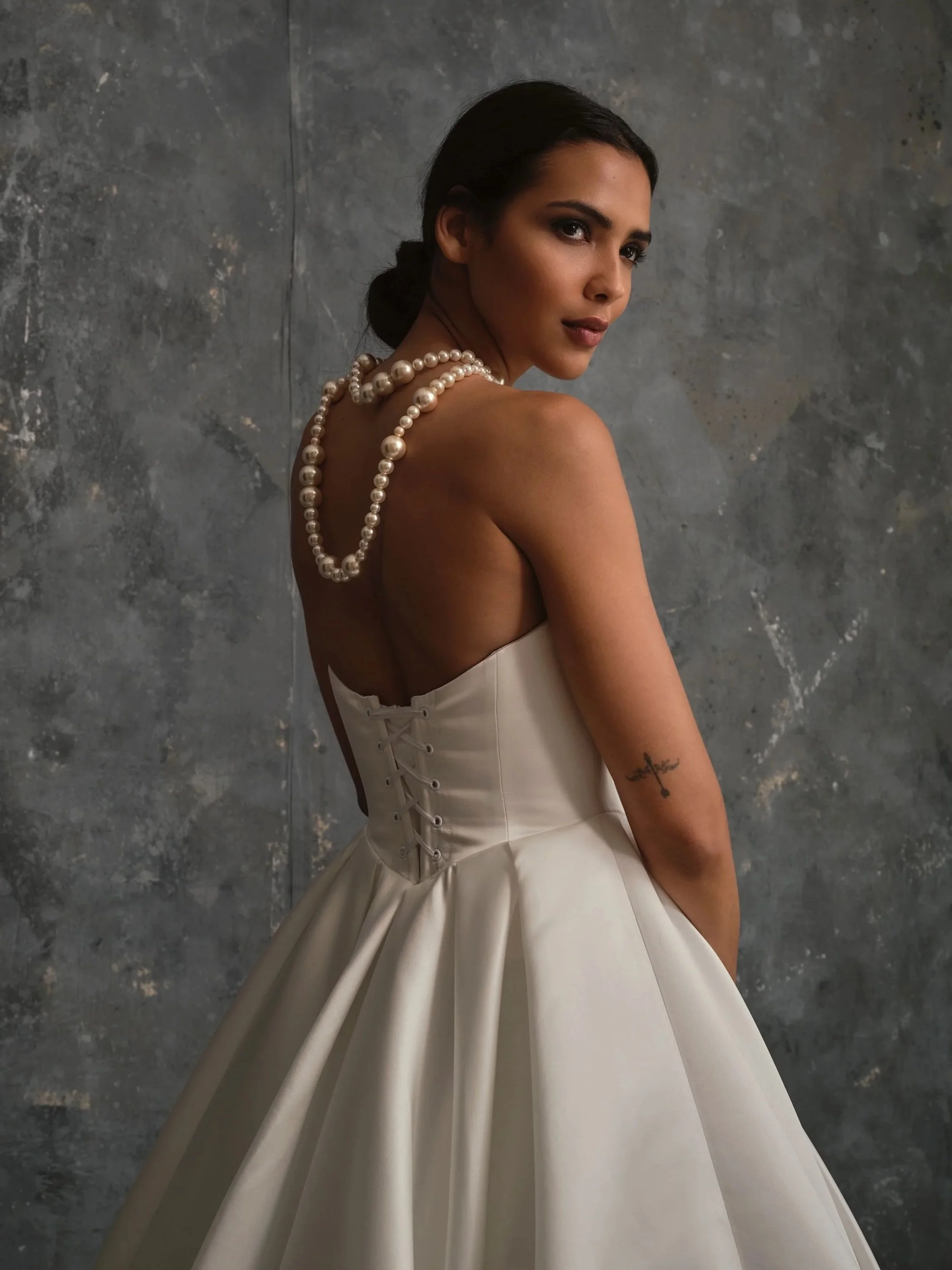 Back view of Celine modern satin wedding dress with corset lace-up back detail, A-line skirt and large pearl necklace