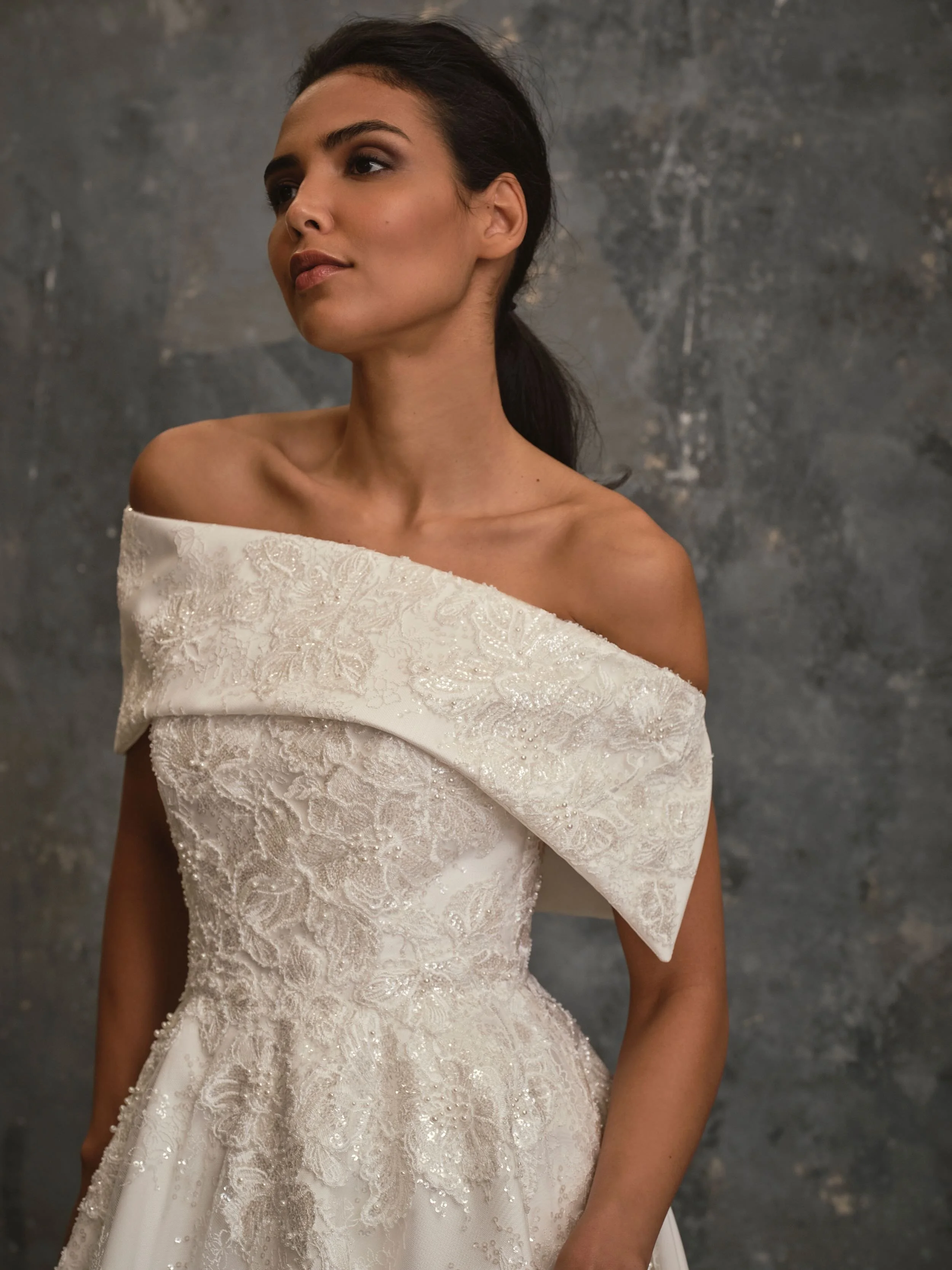 Close-up of Fleur couture wedding dress featuring embroidered lace bodice and asymmetric off-the-shoulder bridal cover