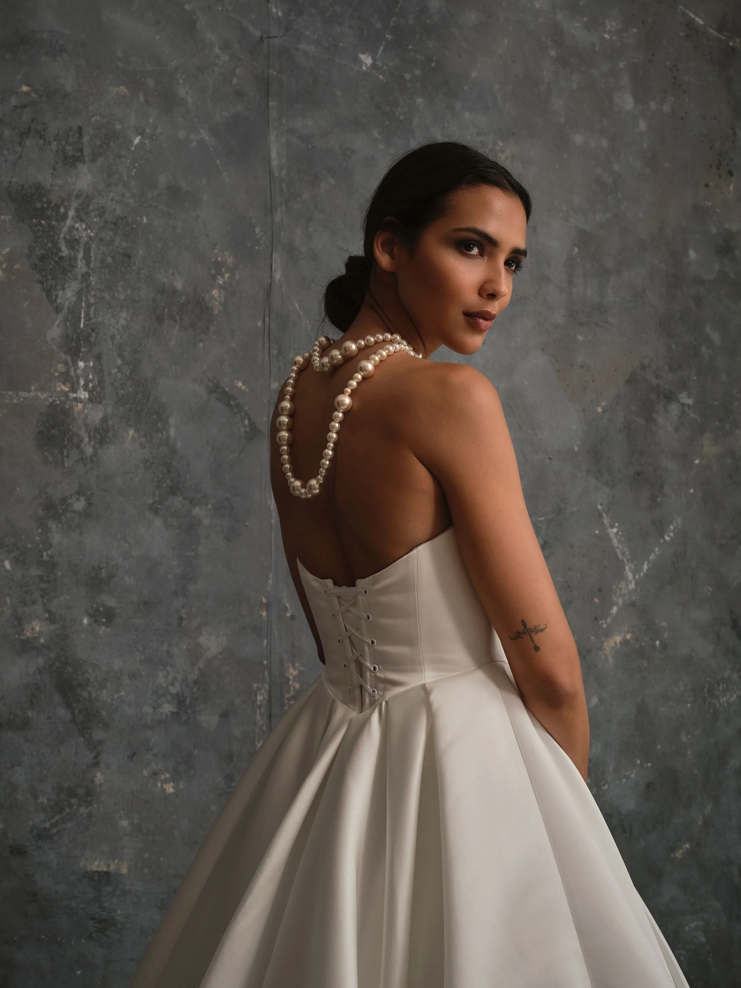 Back view of Celine modern satin wedding dress with corset lace-up back detail, A-line skirt, large pearl necklace