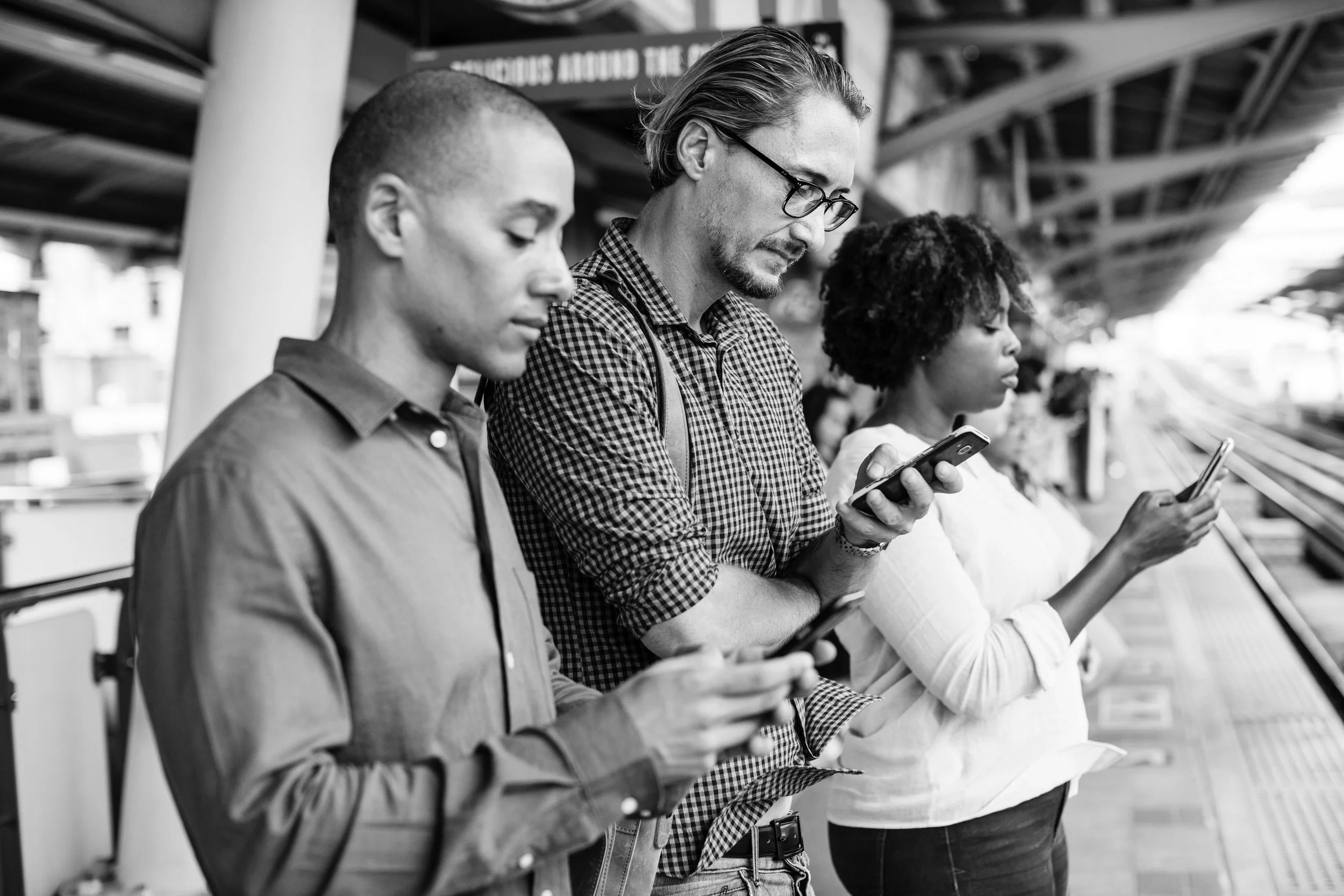 three-adults-using-smartphones-on-train-platform-bw.jpg