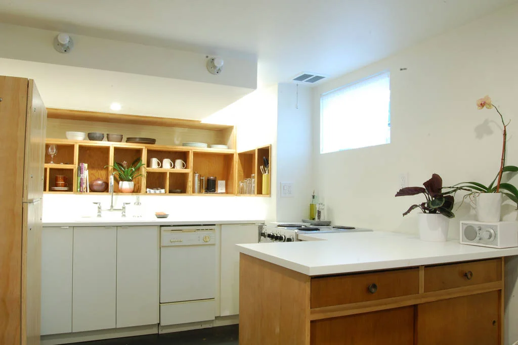 Custom recessed cubbies for storage are made of reclaimed fir wood salvaged from the drawer boxes of an old church kitchen. The wooden cabinet base of the bar is a repurposed piece of mid-century furniture. By removing the back of the piece, there are open shelves accessible from the kitchen side, while the sliding doors on the living room side conceal easy access to board games.