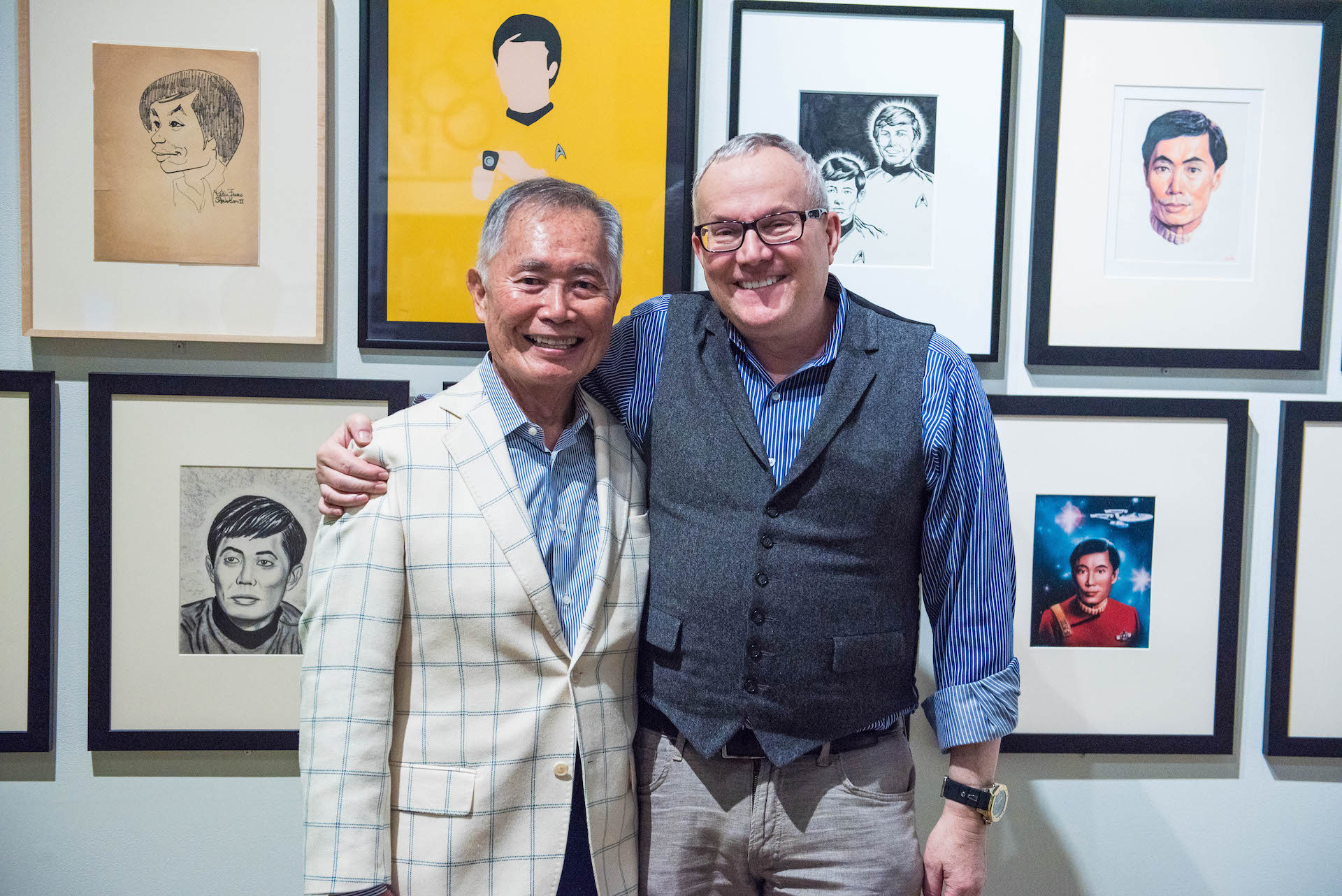 George and Brad Takei grinning in front of fan art.
