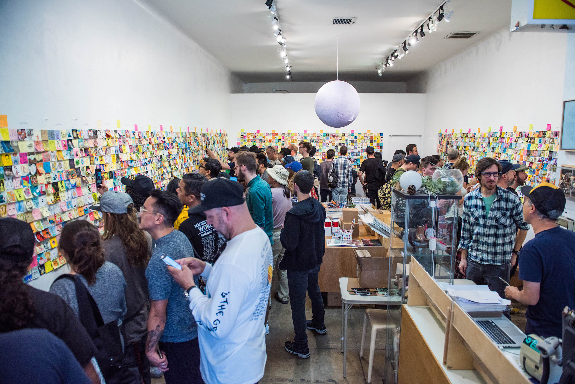 Giant Robot founder Eric Nakamura (right in the yellow-black cap) at the register as patrons jot down the post-its they wish to purchase.