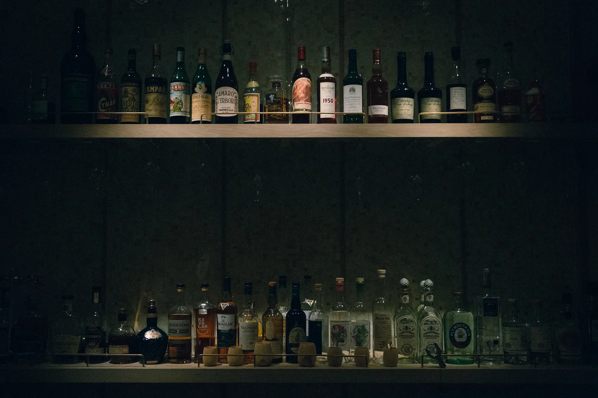At the bar, a m oodily lit wall of spirits rests.