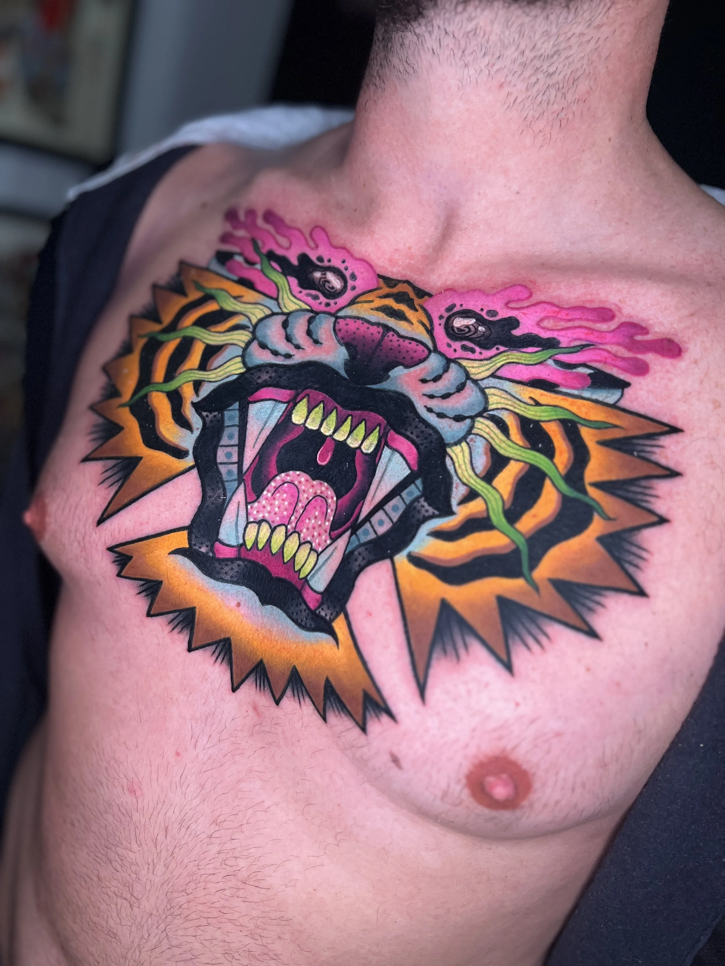 Tattoo of a roaring tiger head with vibrant colors, including pink, orange, green, and black, on a person's chest.