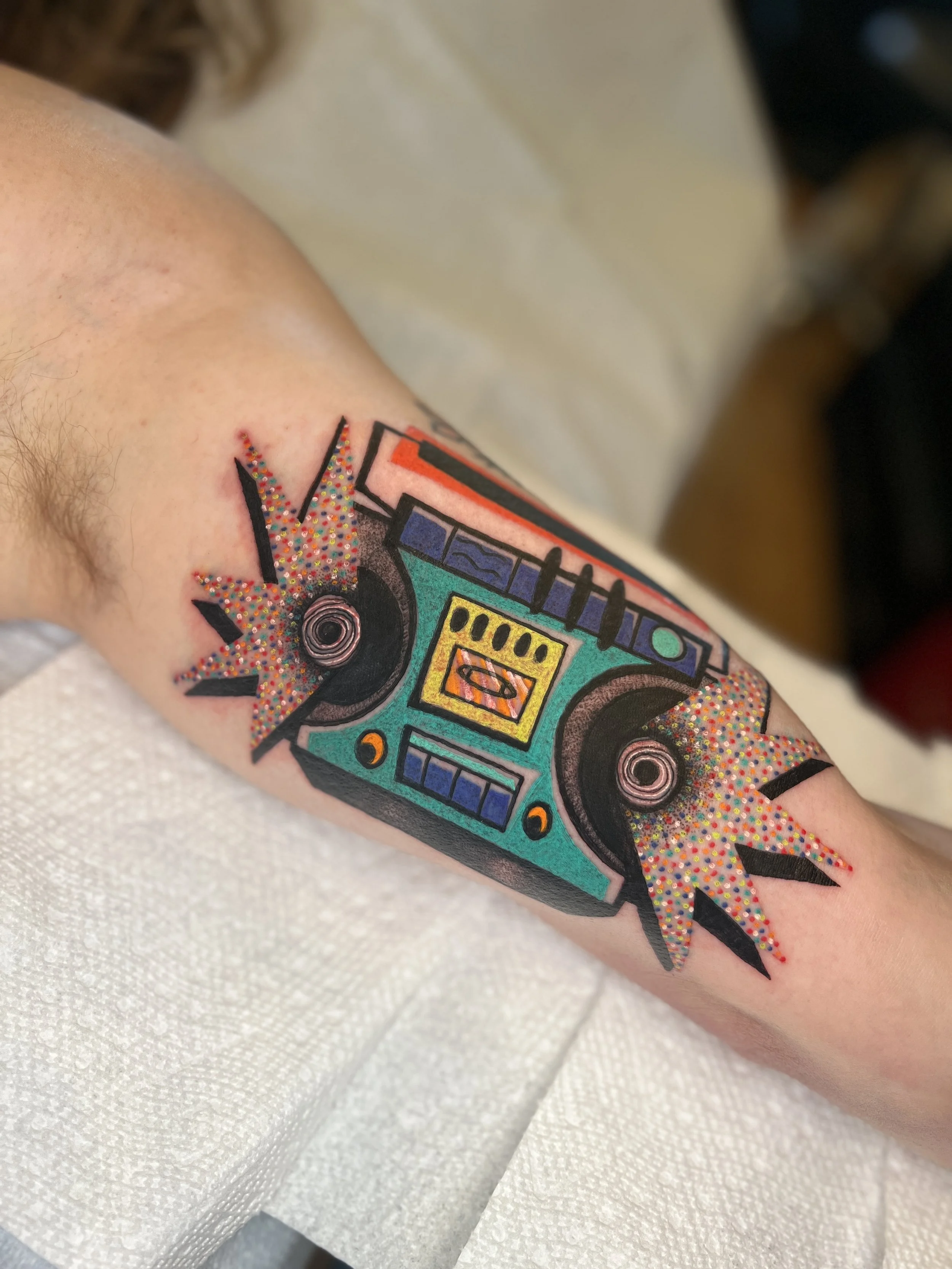 Colorful tattoo of a DJ turntable with speakers and sound waves on a person's upper arm
