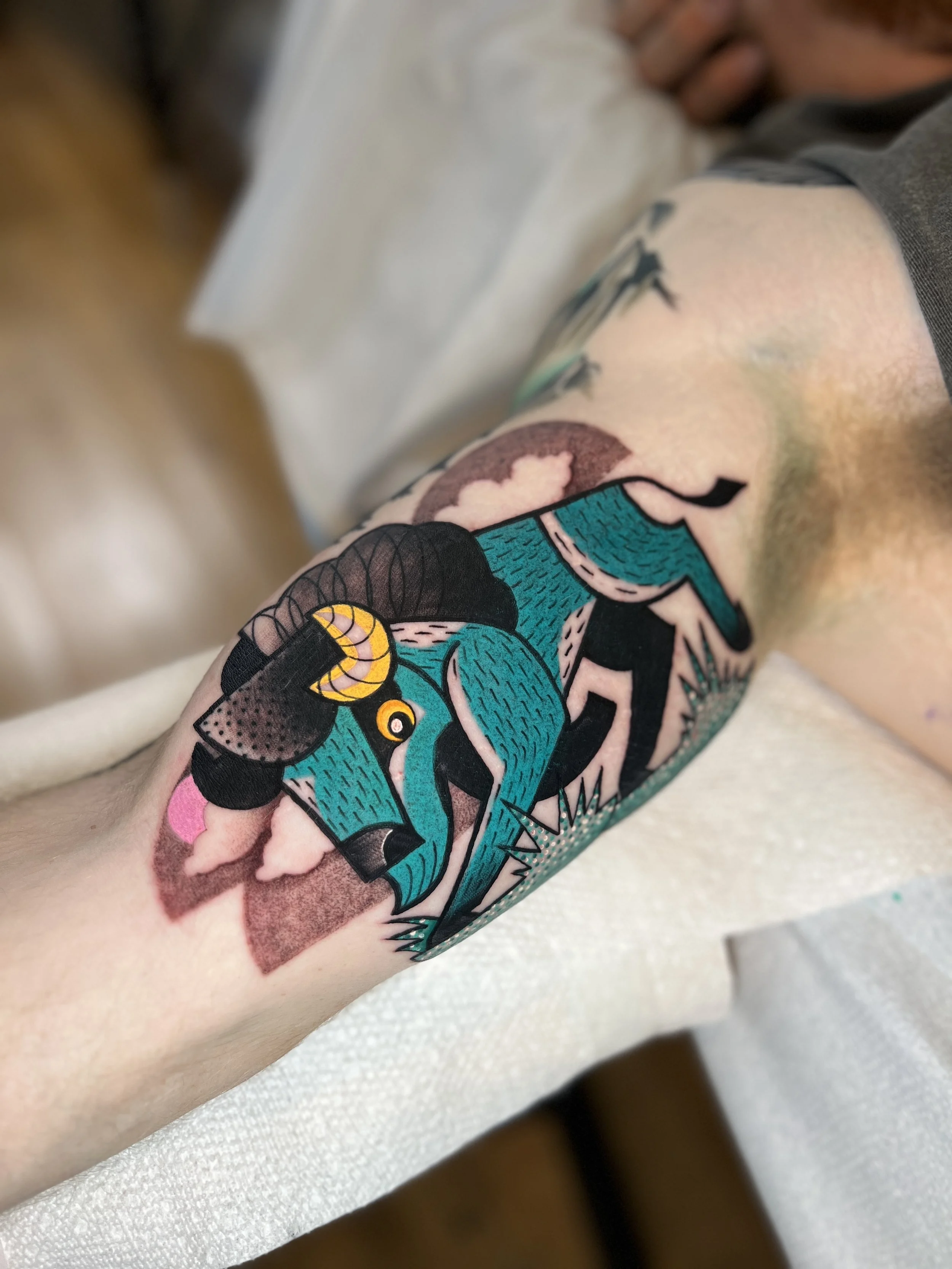 Tattoo of a blue and black stylized bird with yellow accents on person's arm.