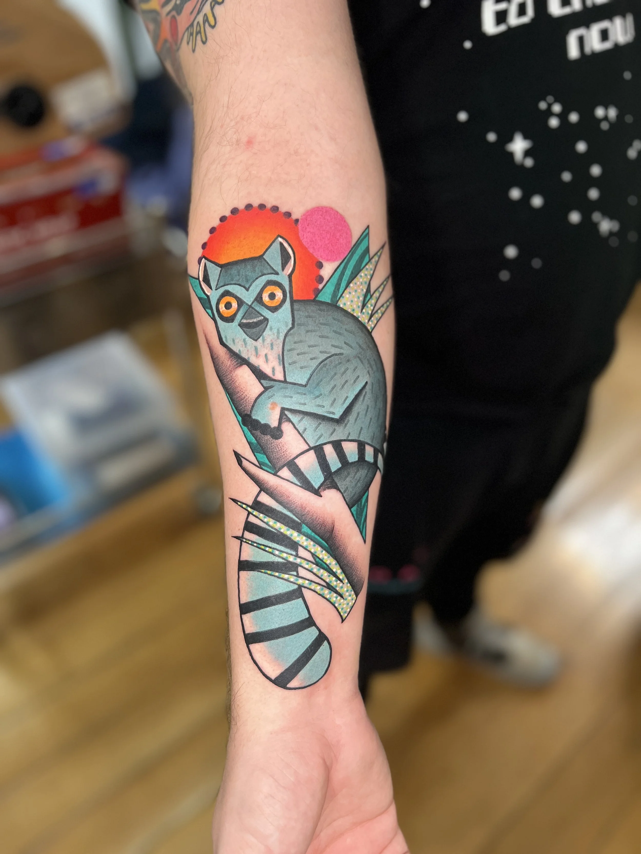 Tattoo of a stylized lemur sitting on a branch with a colorful sunset and abstract leaves in the background.